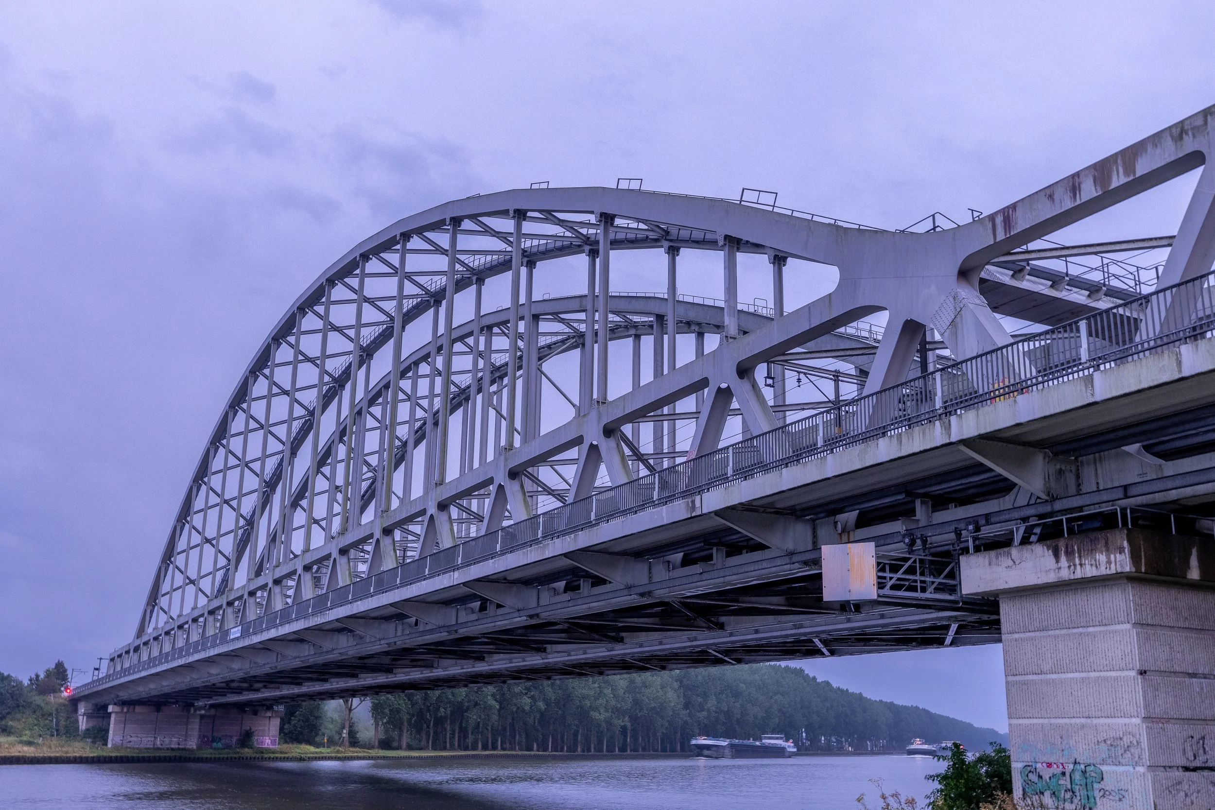 Brug over een rivier met meerdere schepen, onder een bewolkte hemel.