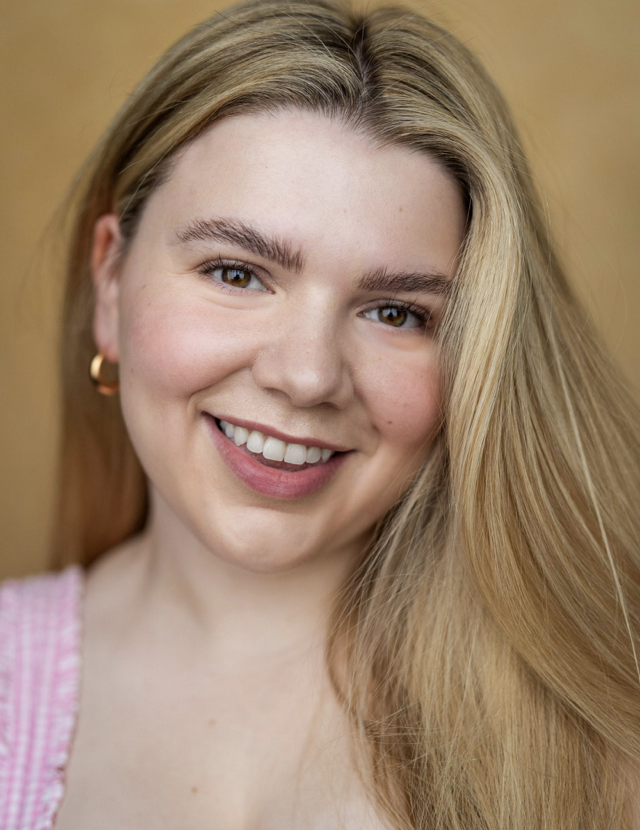 Close-up portrait of a smiling woman with blonde hair, light skin, and wearing a pink top.