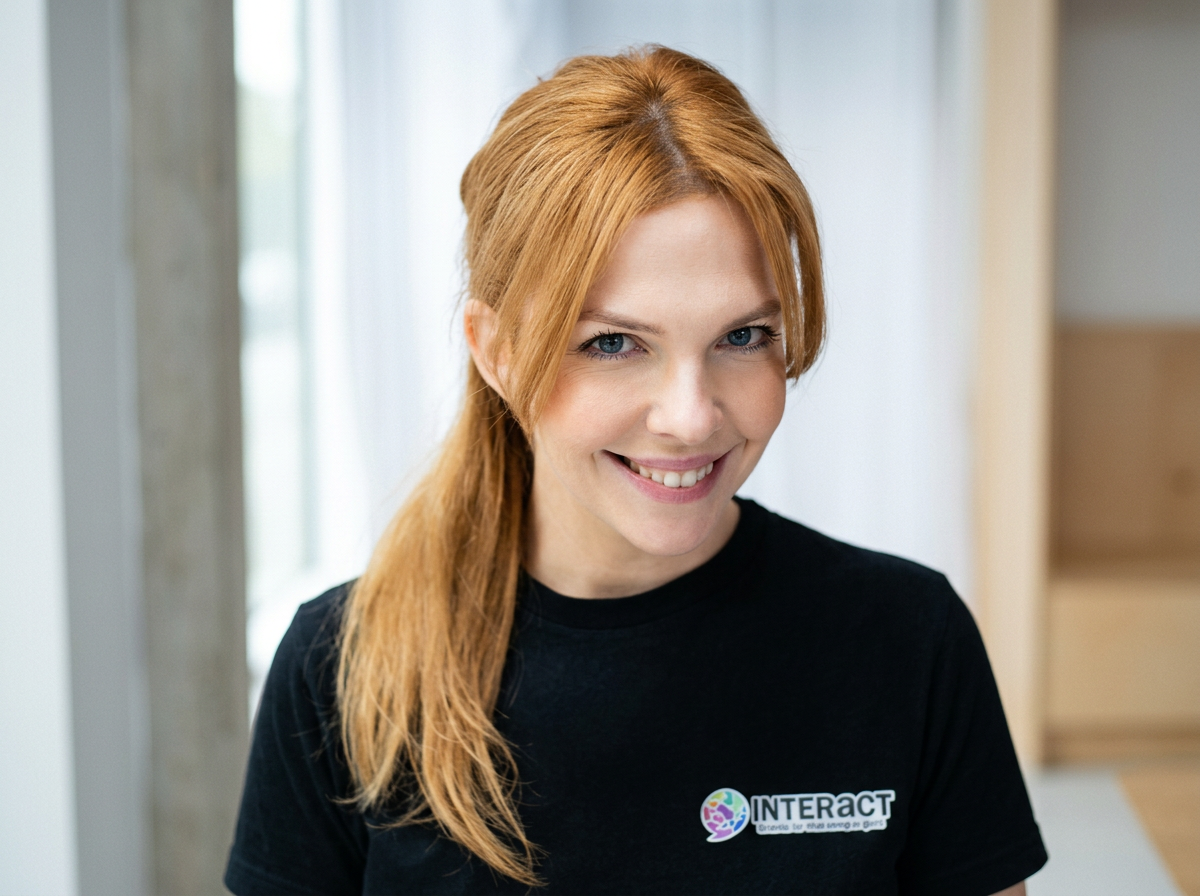 A smiling woman with red hair and blue eyes wearing a black T-shirt with the company logo for 'INTERACT'.