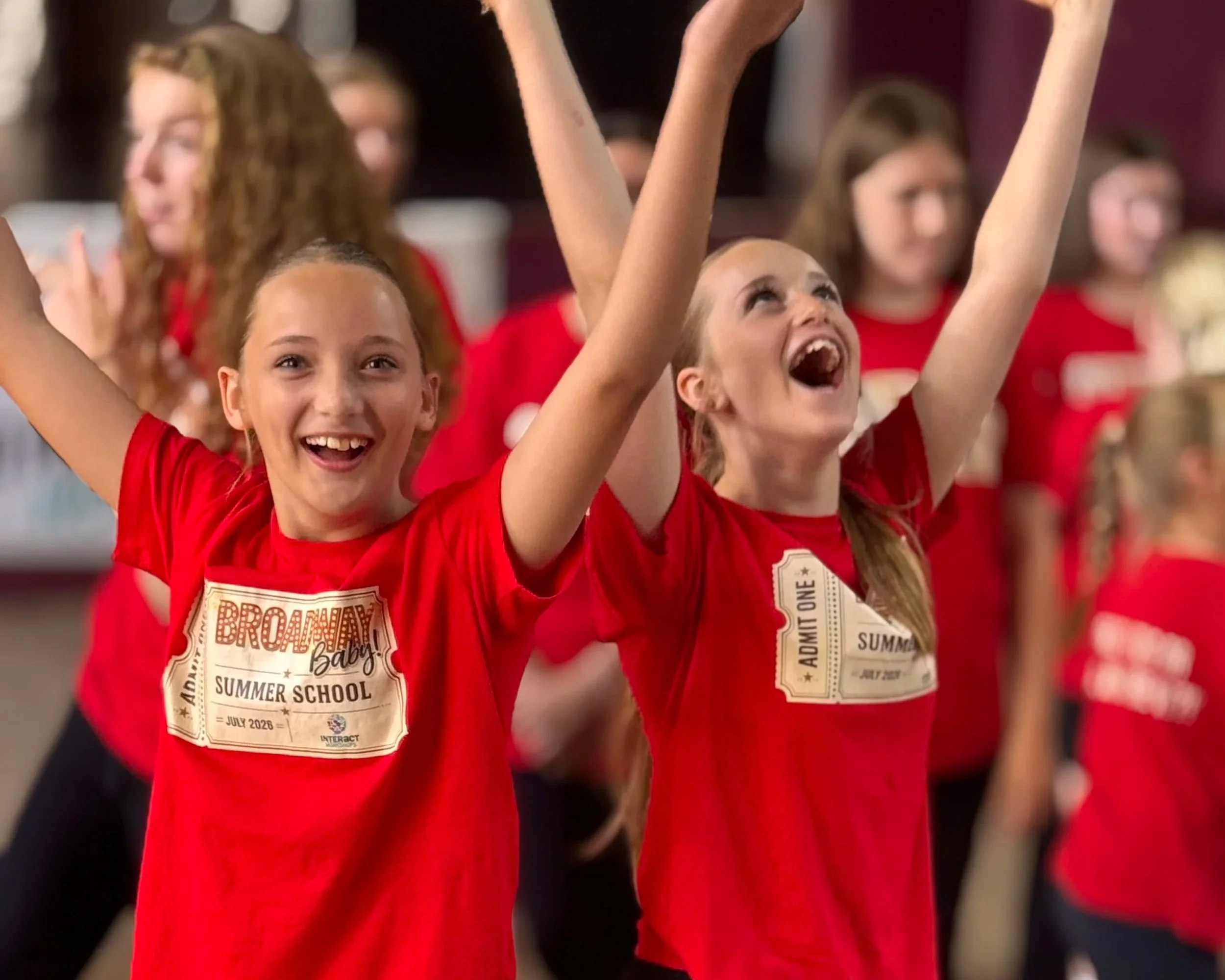 Children wearing red shirts celebrating at summer school event with excitement and joy.