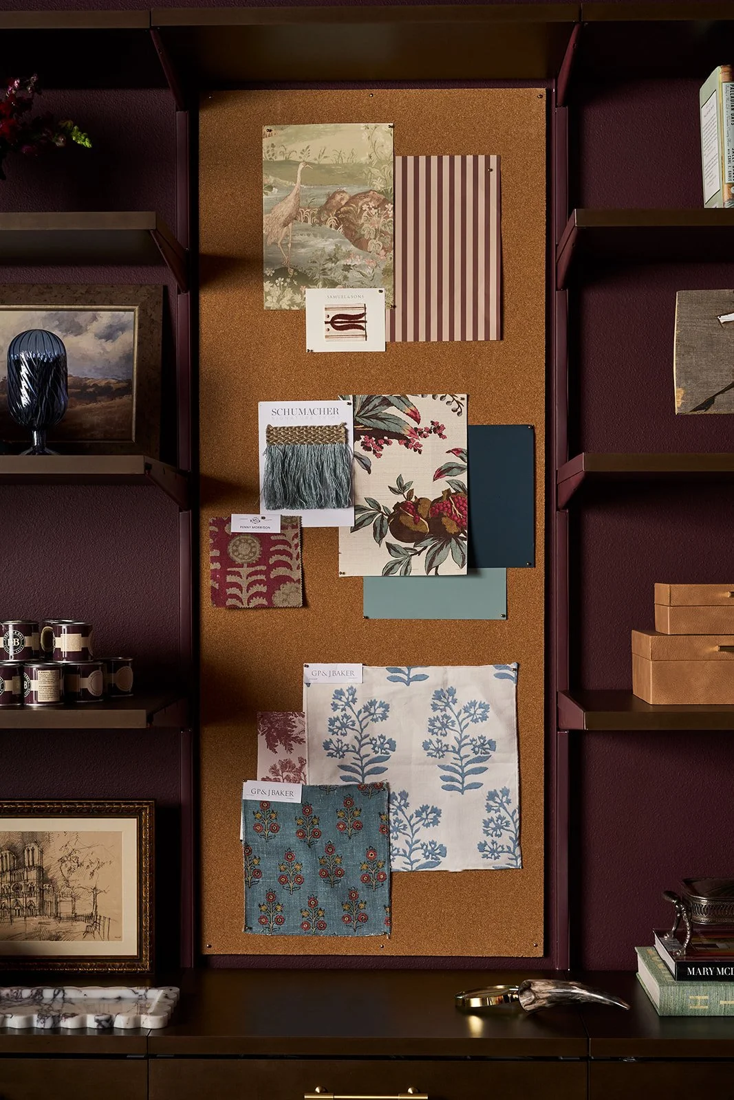 Decor and fabric swatches on a cork bulletin board, surrounded by shelves with books, artwork, and decorative objects.