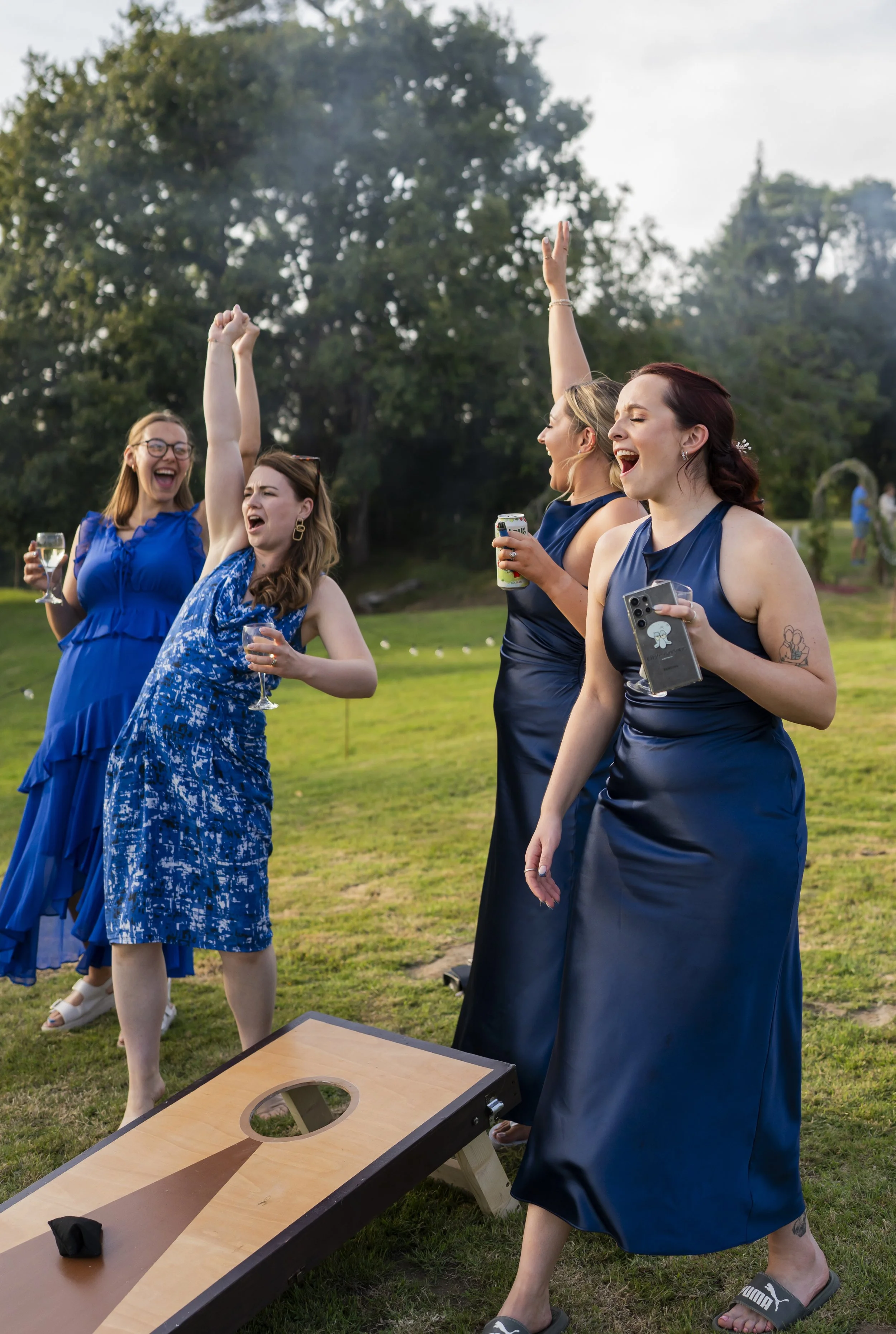 Group of women in blue dresses playing cornhole outdoors, laughing and celebrating.