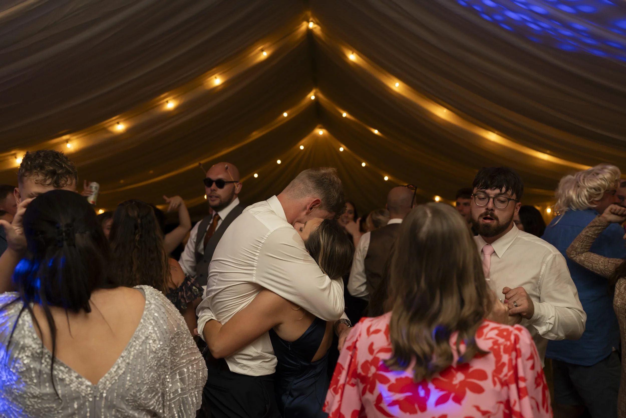 People dancing and celebrating under a decorated tent with warm lighting.