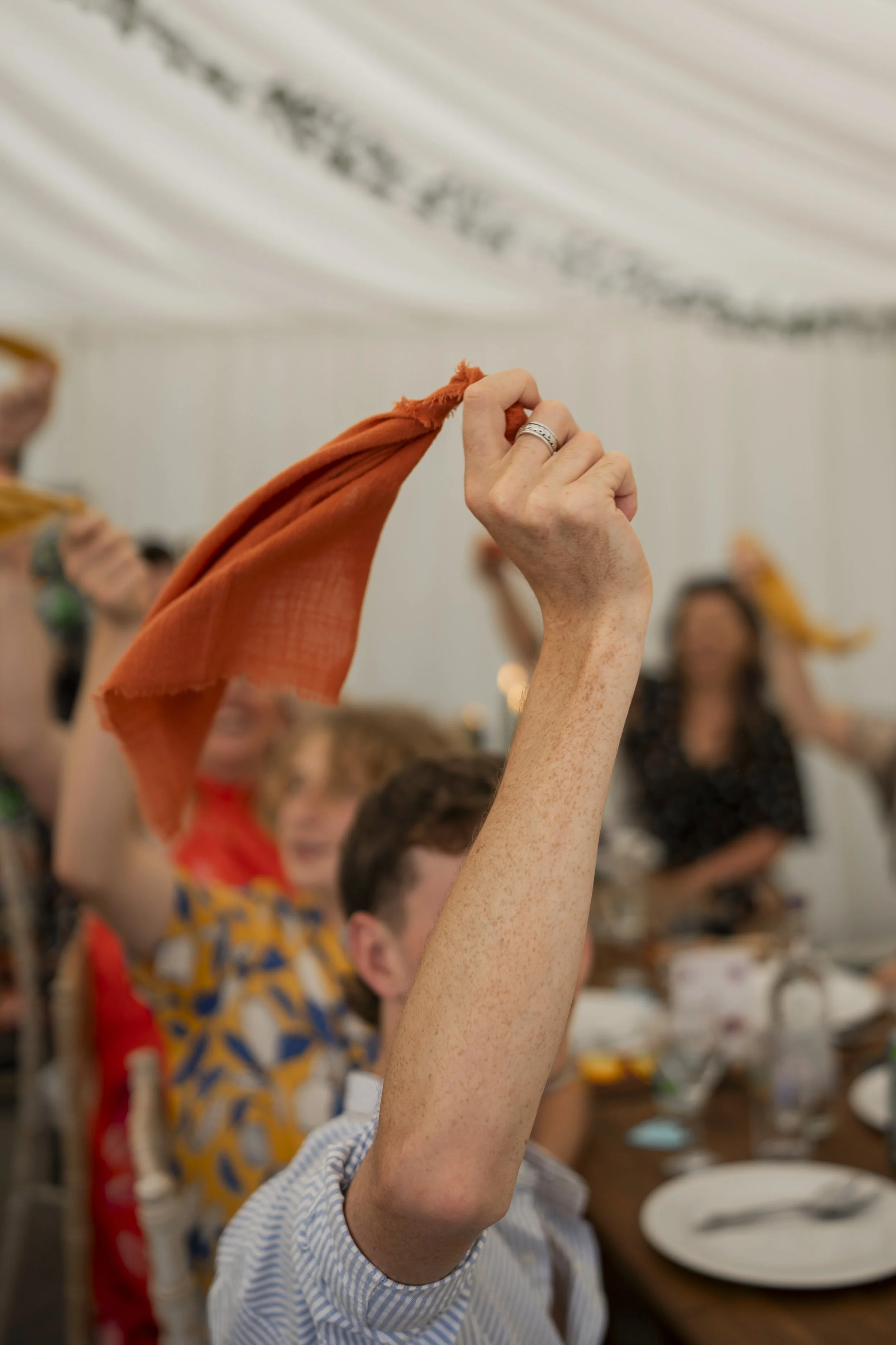 Person raising hand with orange cloth during a group activity in a room with blurred background and other participants.