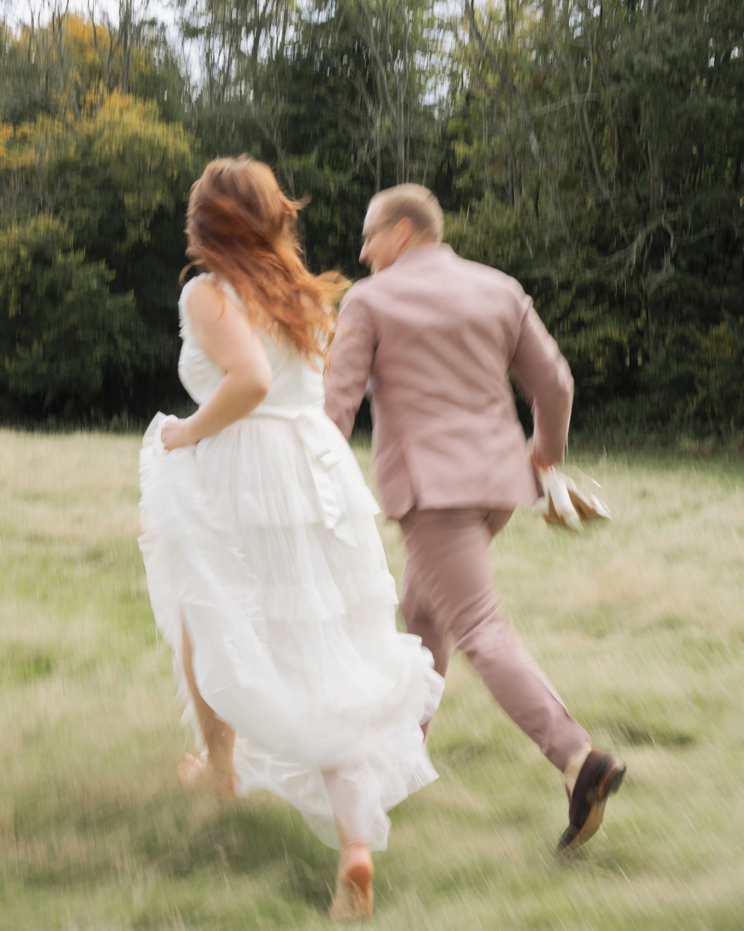 A couple running outdoors on a grassy field with trees in the background, captured with motion blur.