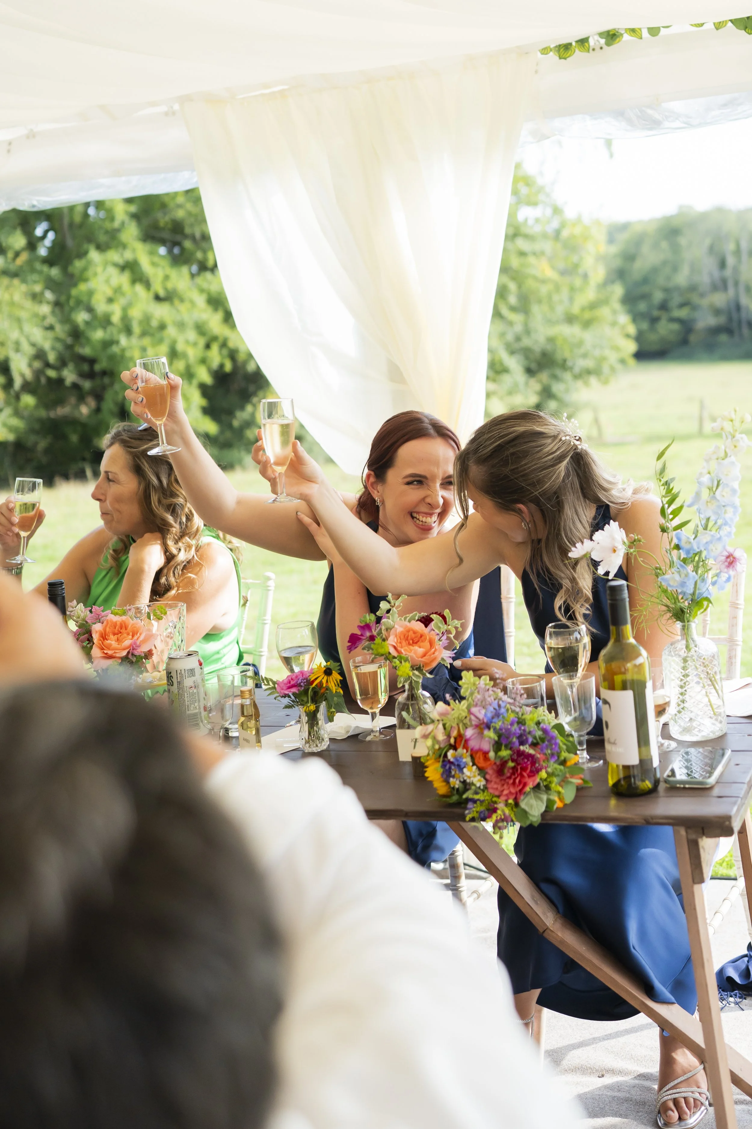 Women celebrating at an outdoor wedding reception, raising glasses of champagne and smiling.