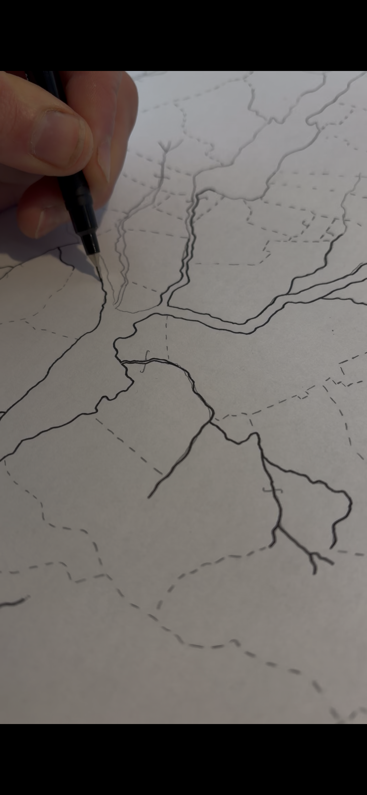 A person drawing map boundaries with a black pen on a large sheet of paper, showing states and regions outlined with dashed and solid lines.