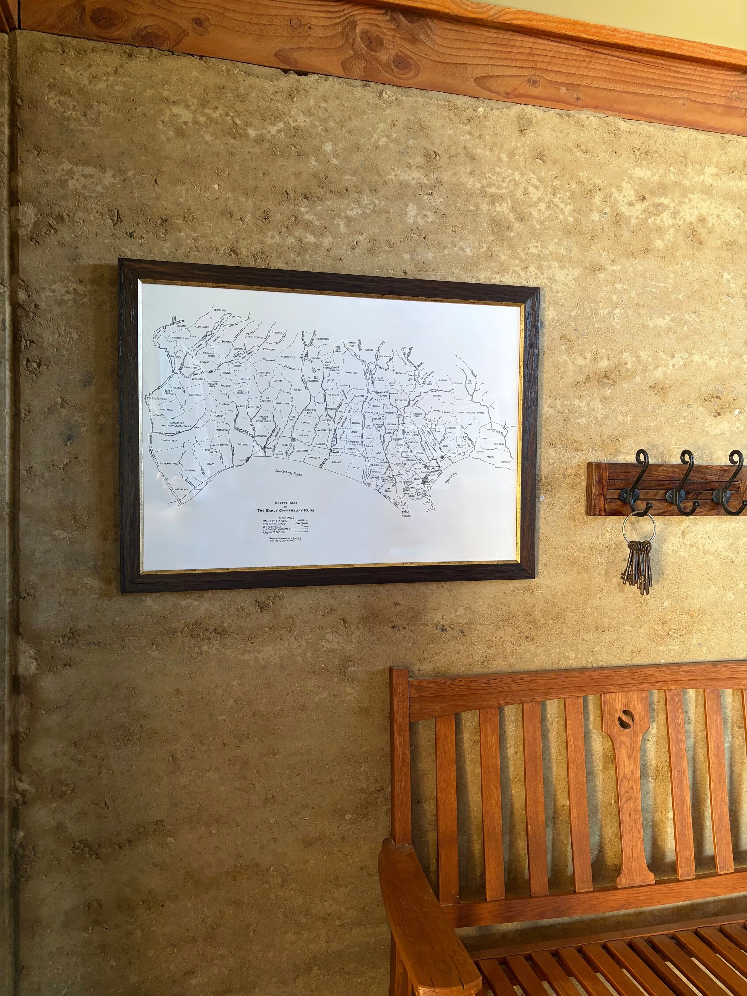 A framed black-and-white map on a textured beige wall, with a wooden coat rack holding keys nearby.