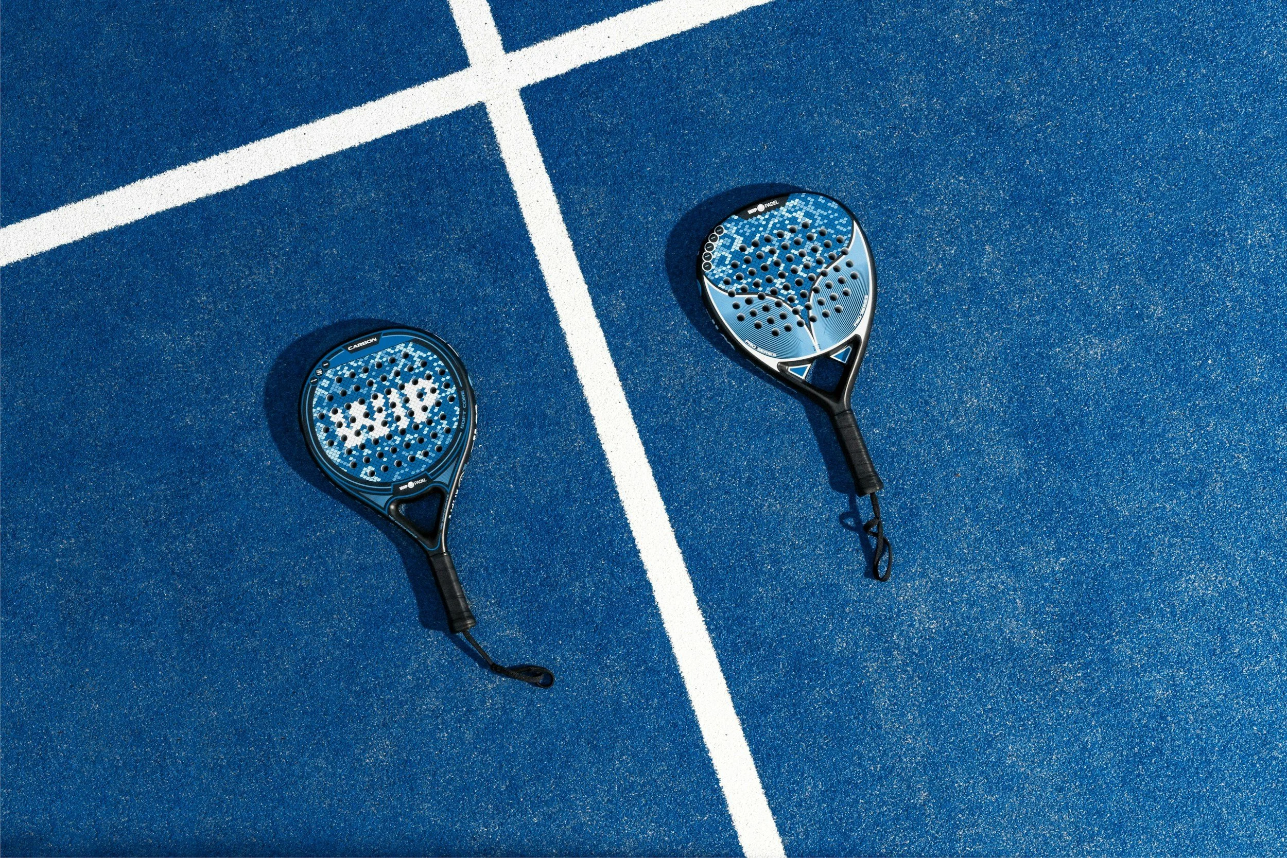 Two blue padel rackets lying on a blue court with white boundary lines