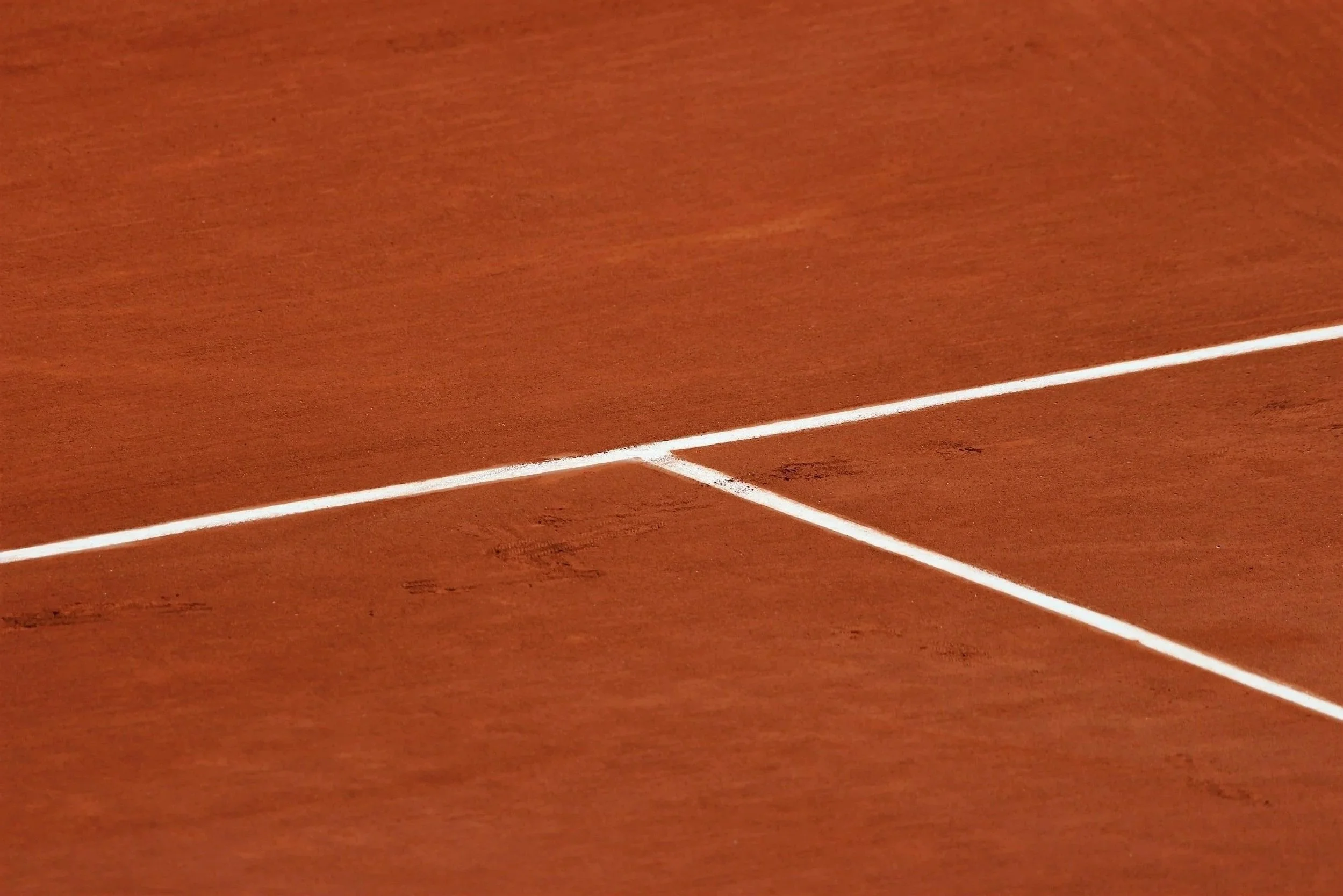 Close-up of white court lines on a red clay tennis court