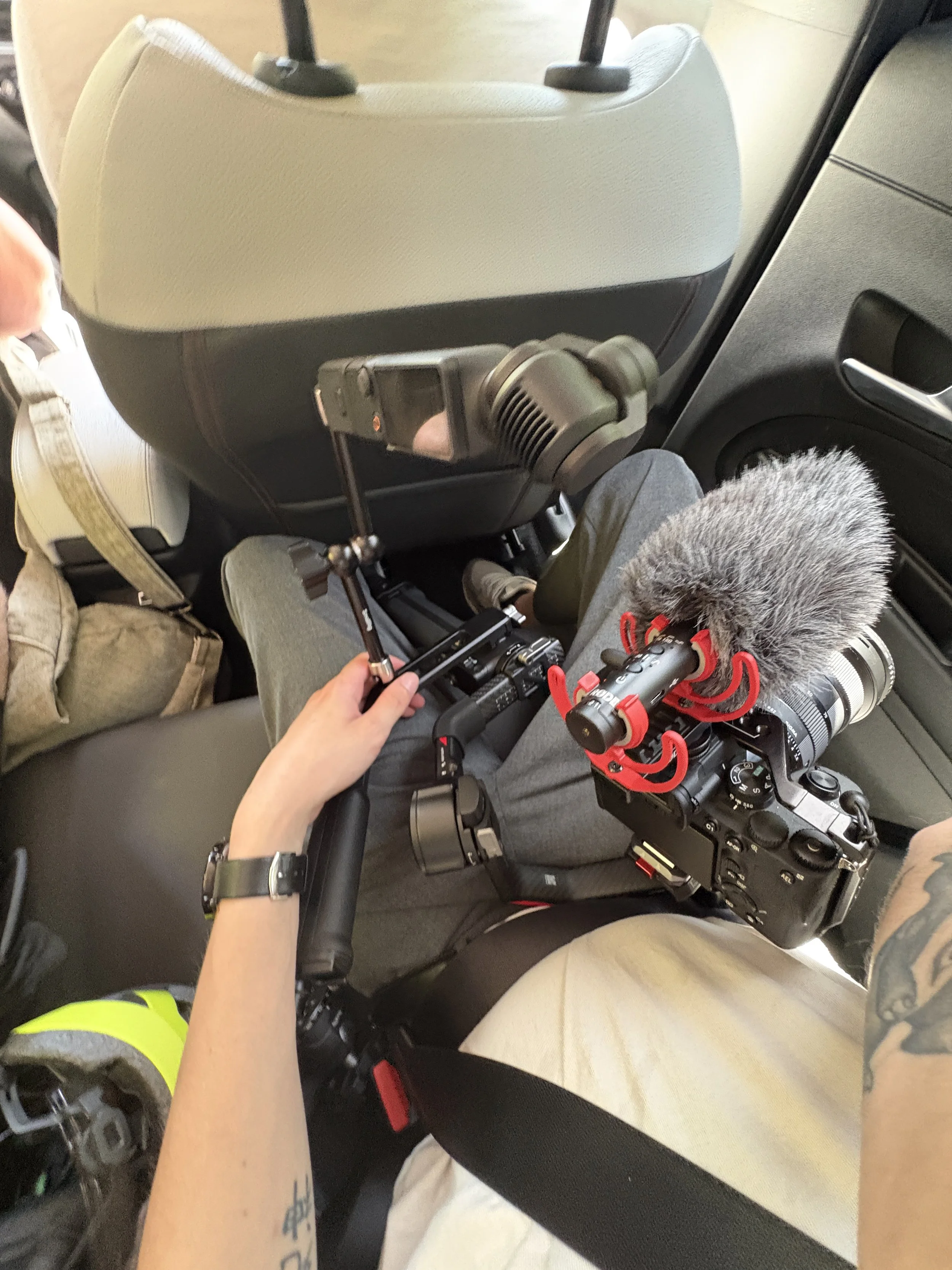 Un homme avec une veste à manches courtes portant une montre regarde un caméscope dans une voiture, avec un microphone attaché à son équipement.