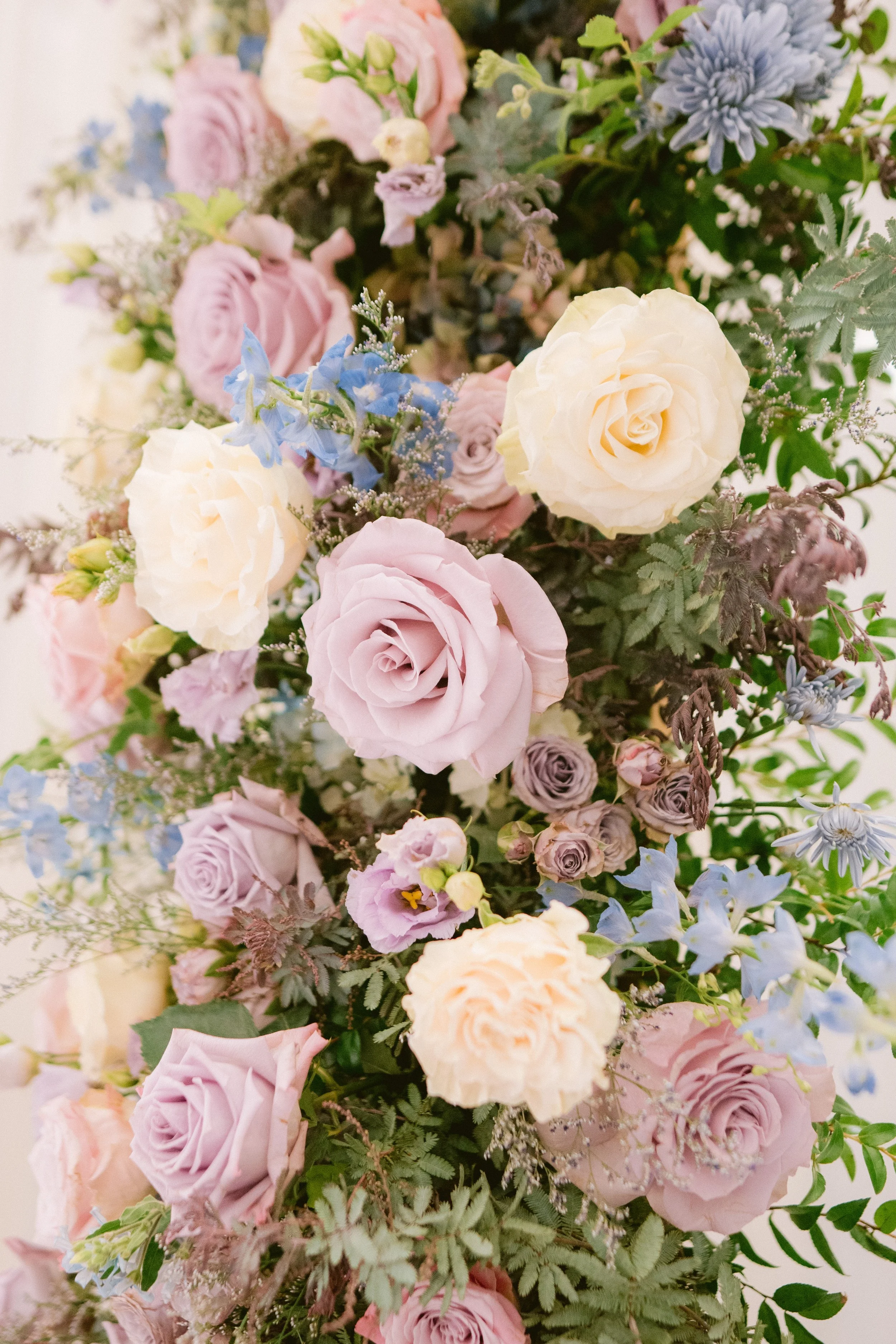 A vibrant and colorful bouquet of various flowers including roses, blue delphiniums, lisianthus, and greenery.