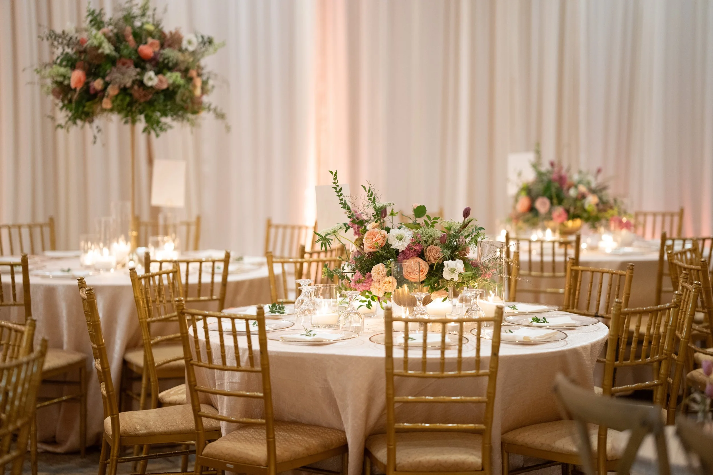 Elegant banquet table with floral centerpieces and gold chairs at a wedding reception.
