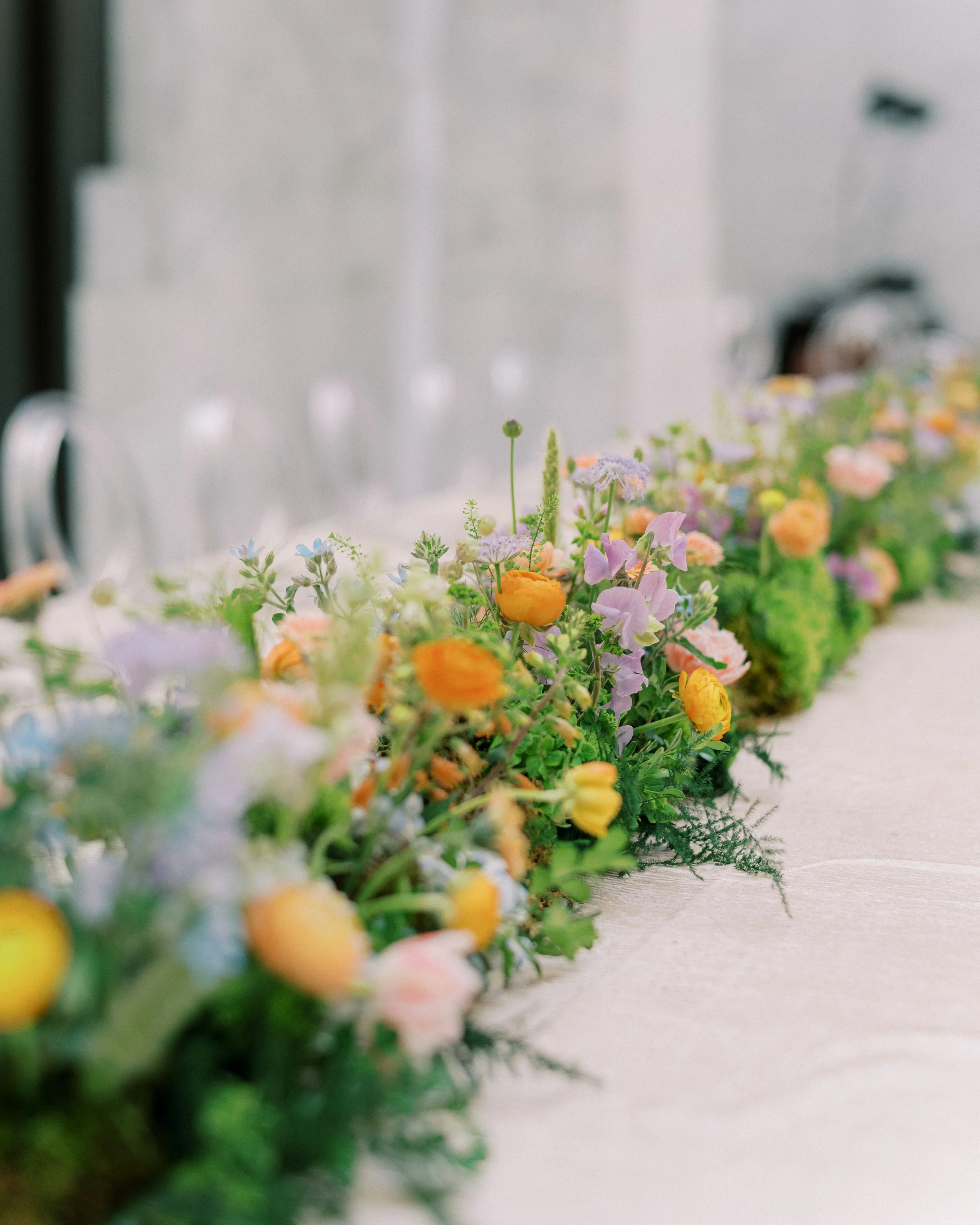 A close-up view of a colorful flower arrangement on a light-colored table, with blurred background.