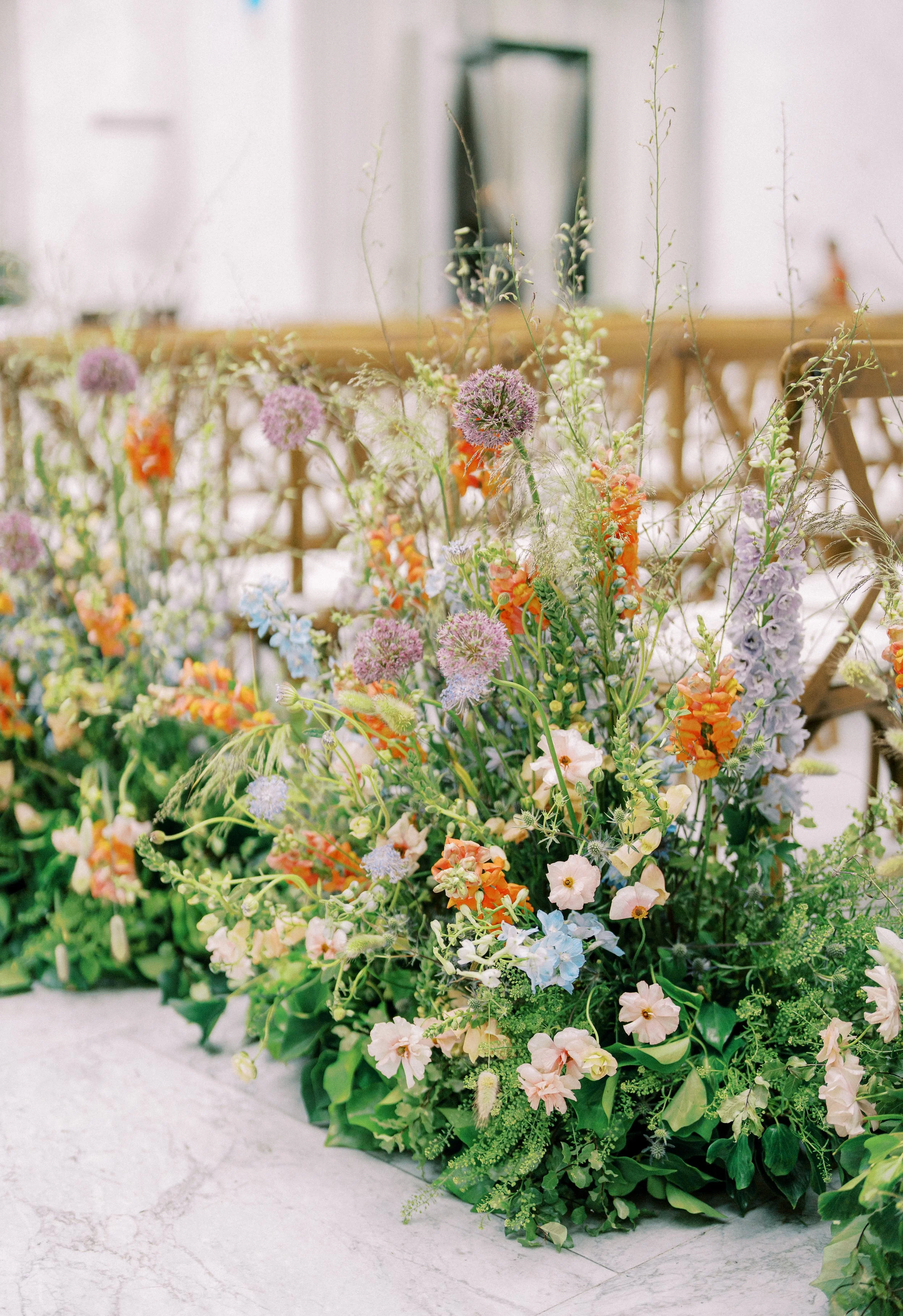 A large floral arrangement with various colorful flowers, including pink, orange, purple, and white, set on a marble surface in an indoor setting.