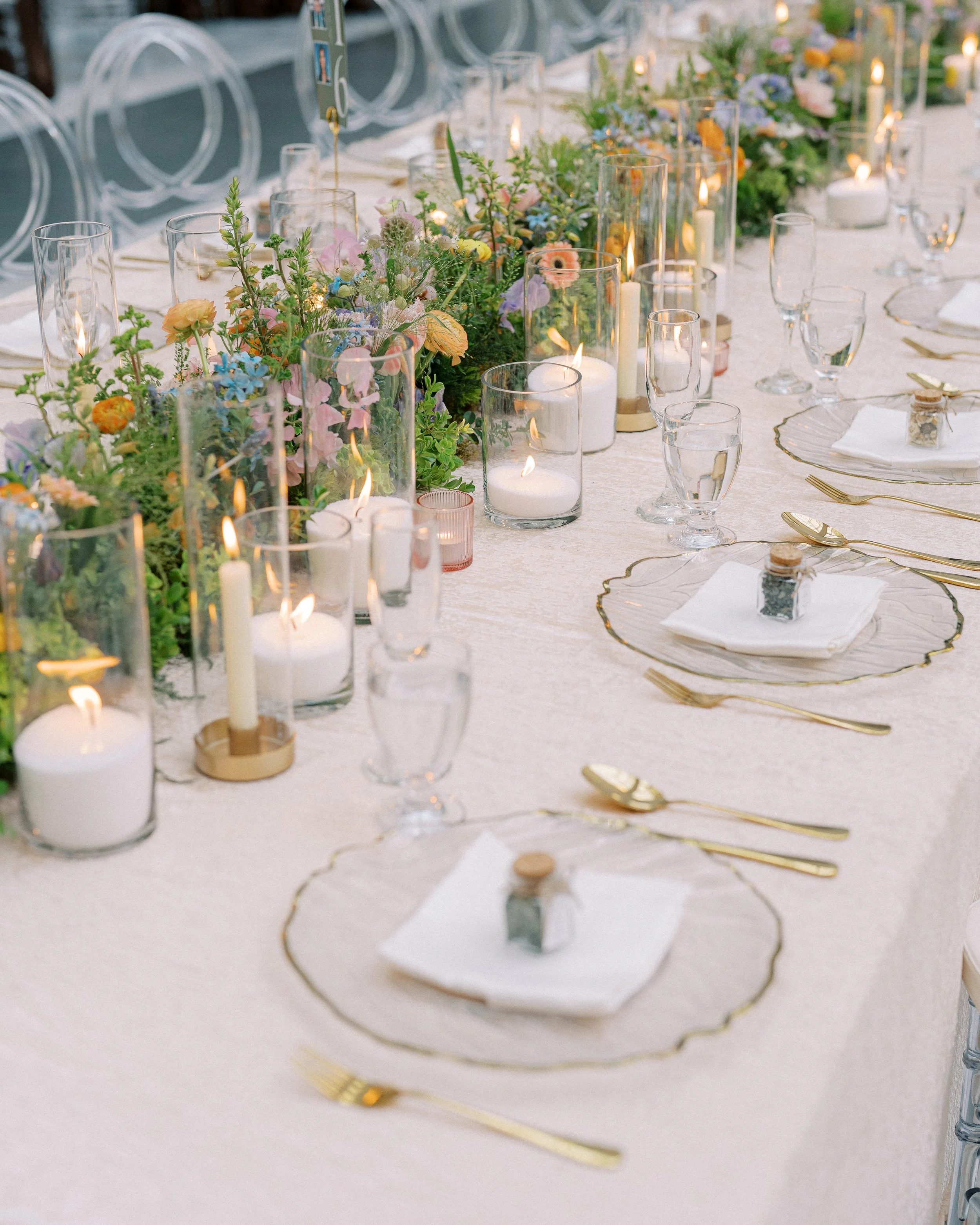 A long dining table decorated with a floral centerpiece, candles in glass holders, and gold cutlery, set for a formal event.