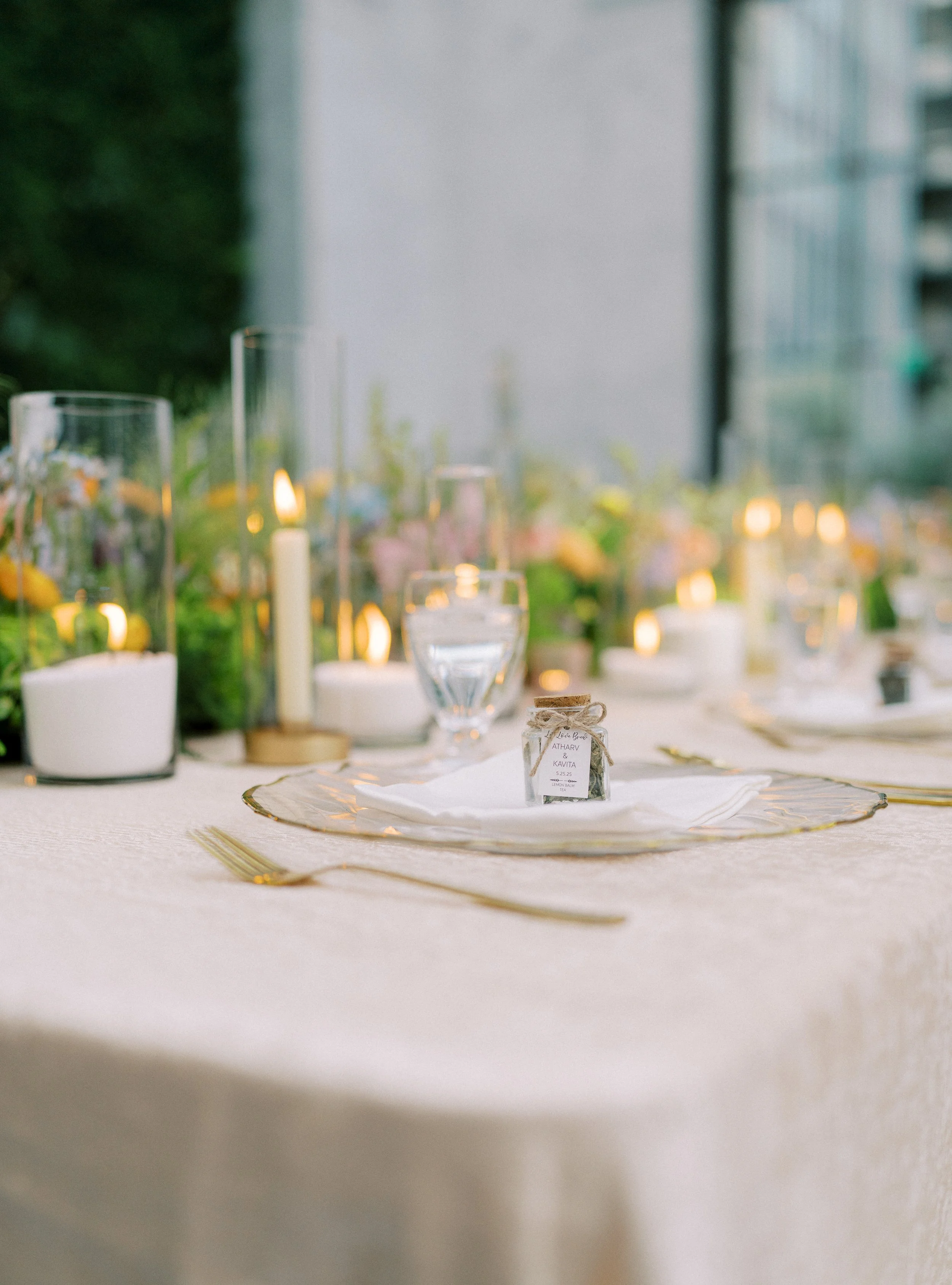 Decorated table with candles, colored flowers, and small bottles, set for an event, with blurred city building background.