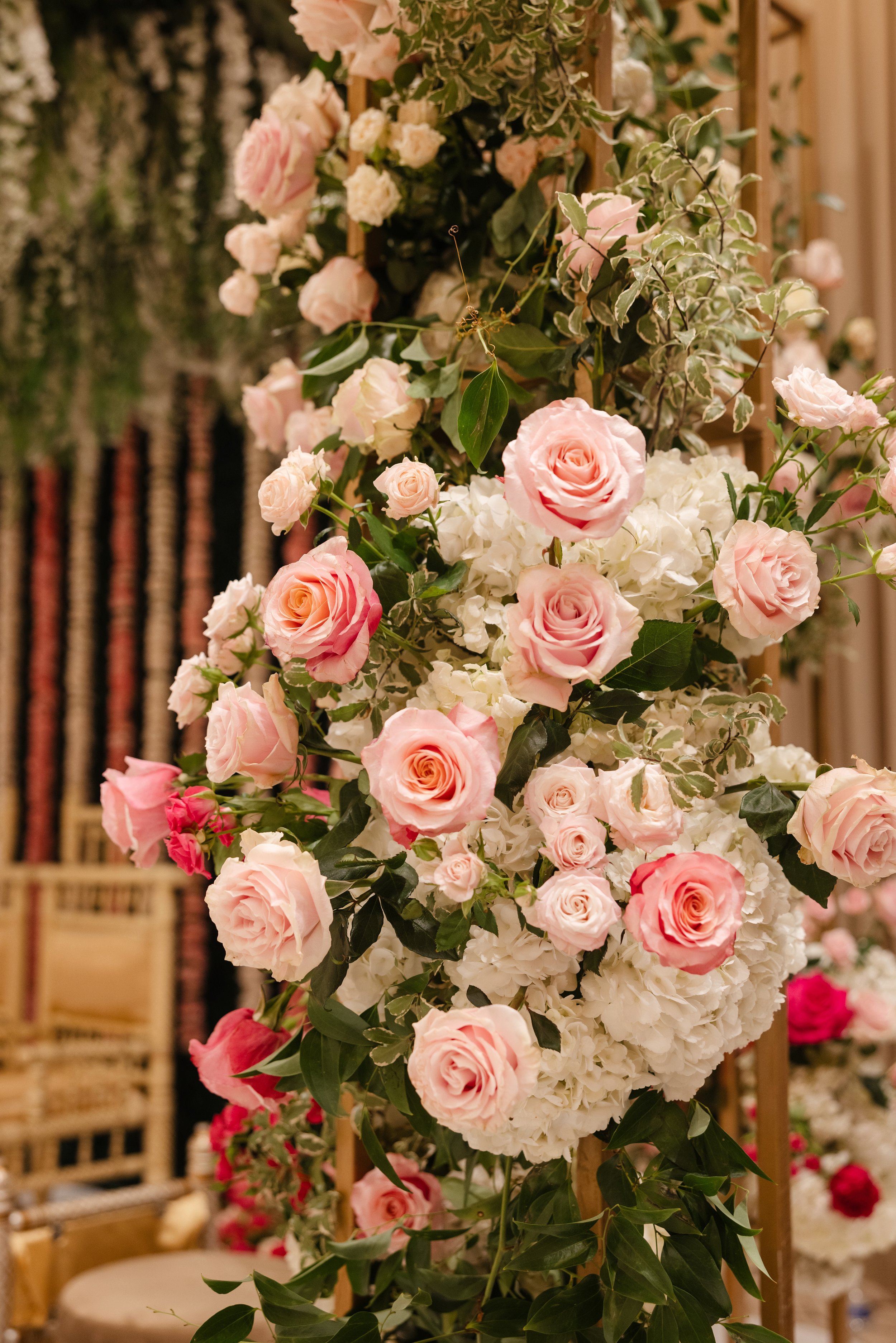 A floral arrangement featuring pink roses and white hydrangeas, with greenery, on a wooden stand at a flower shop or event setting.