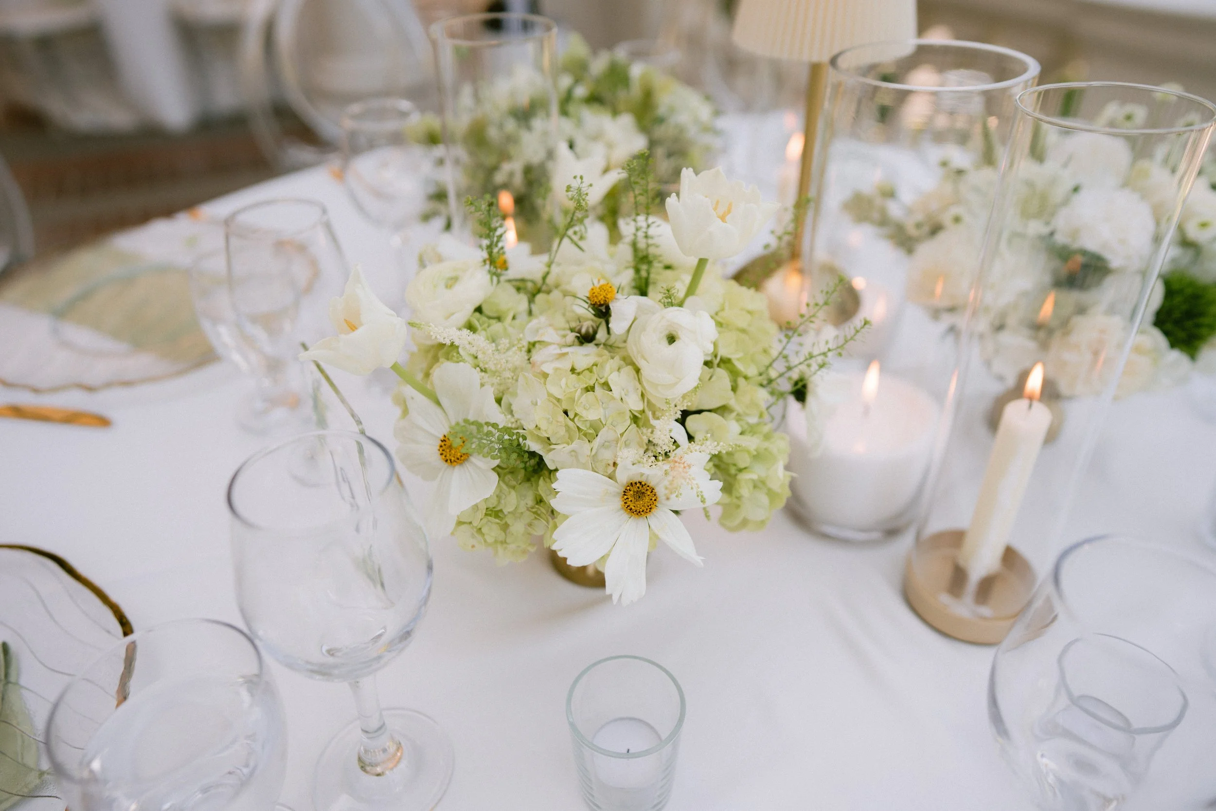 Elegant table centerpiece of white flowers and candles on a white tablecloth.