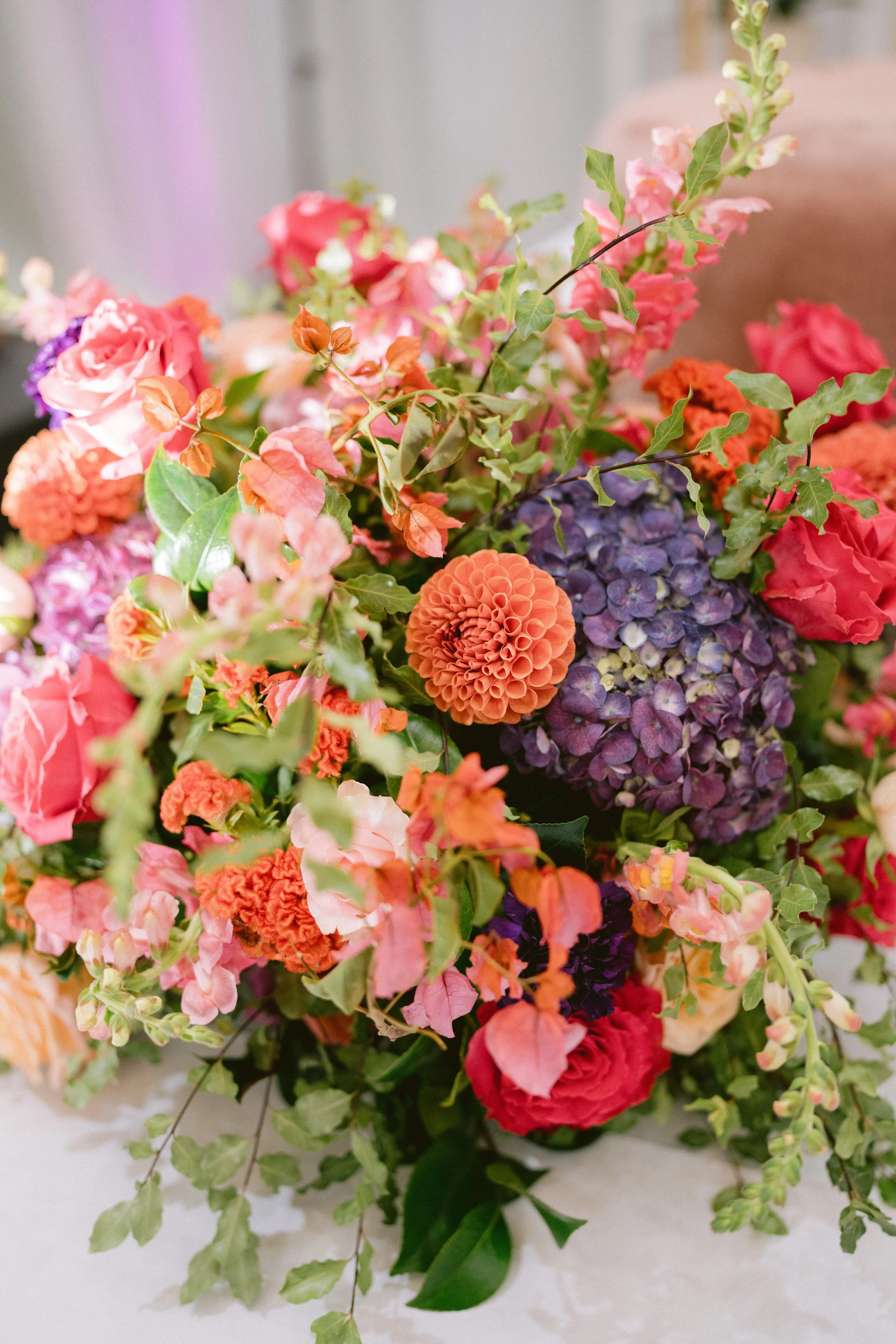 A colorful bouquet of various flowers including roses, hydrangeas, and other blooms with green foliage on a light background.