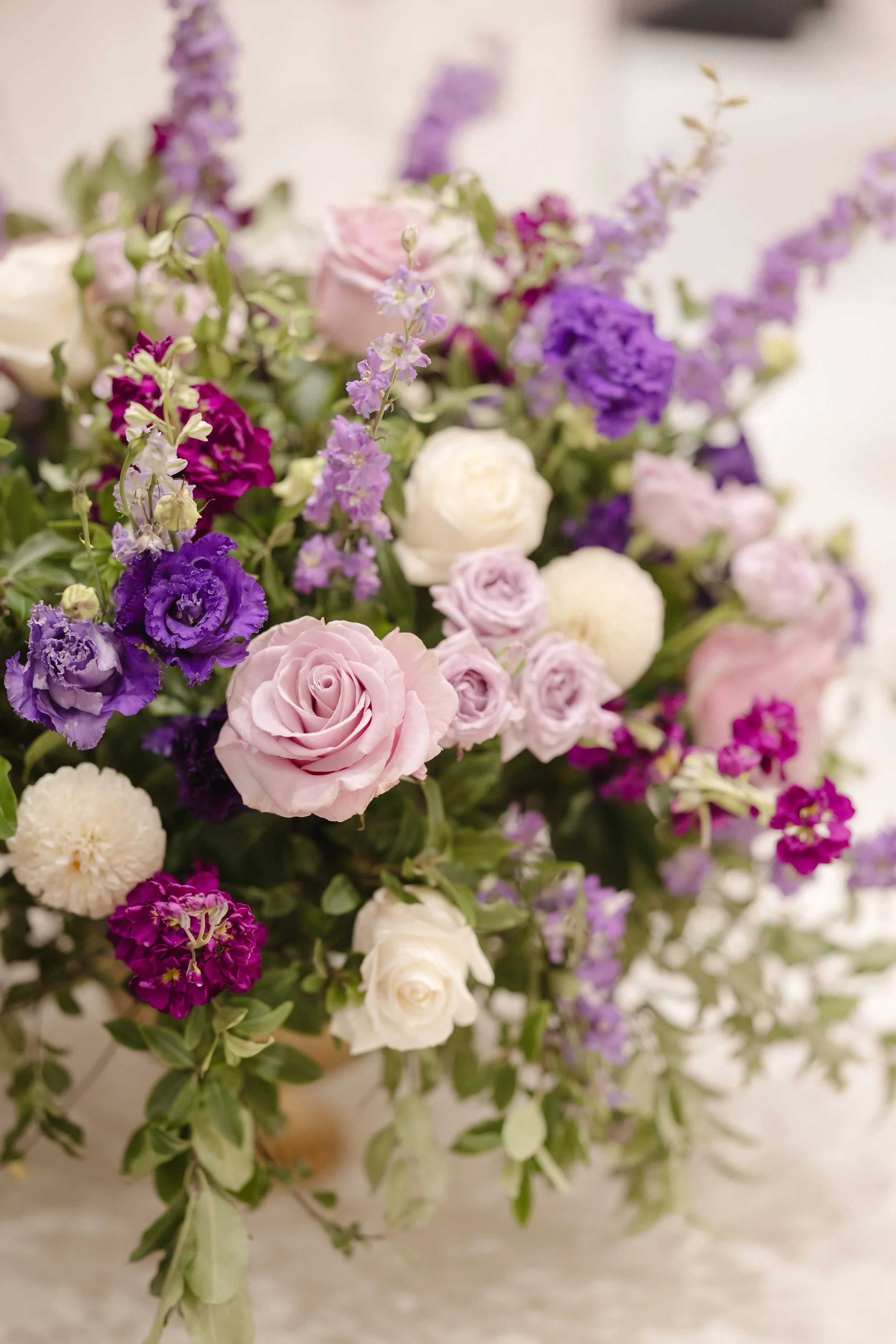 A bouquet of mixed flowers including pink roses, white roses, purple lisianthus, and purple statice flowers with green foliage.