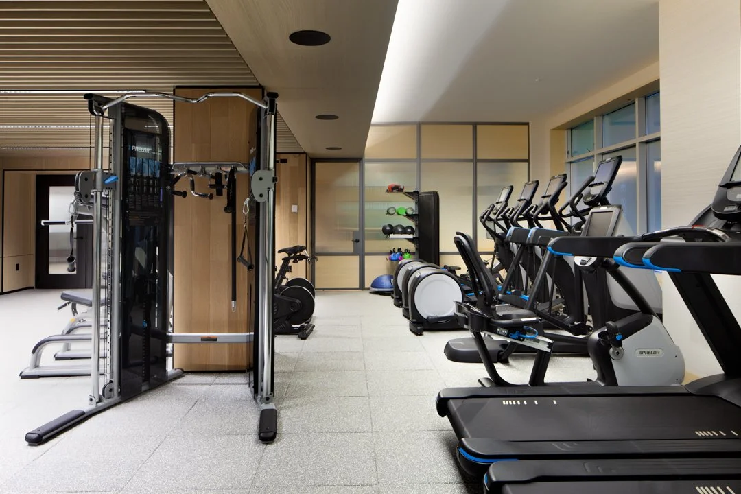 Empty gym featuring cardio machines, weightlifting equipment, and a rack of exercise balls and weights.