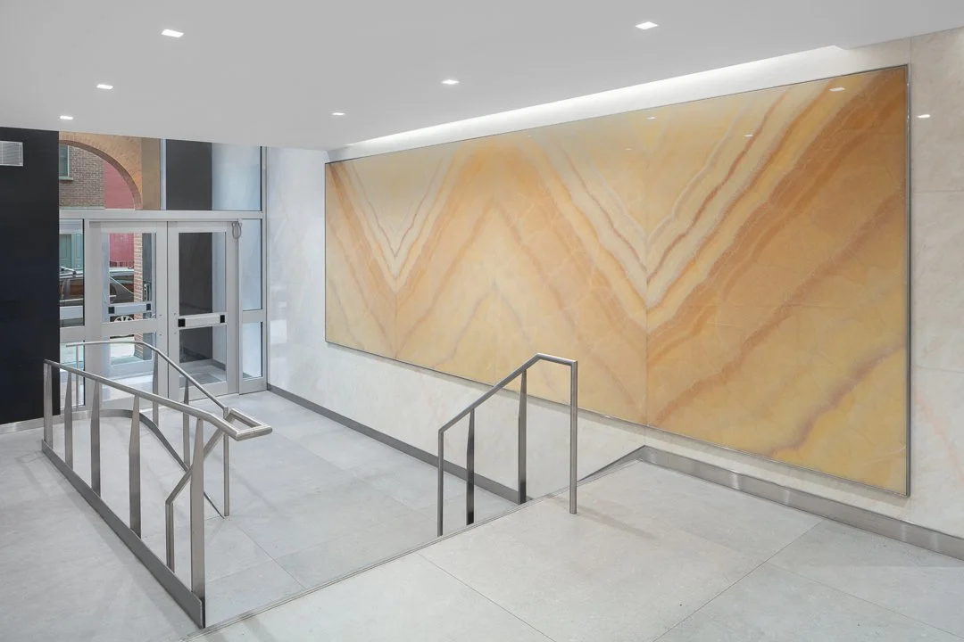 P661 - Unique wall art installation that looks like 4 symmetrical panels of a veined stone in warm tones which complement a cooler white and grey tile entrance with stairs and brushed nickel railings and steel and glass doors