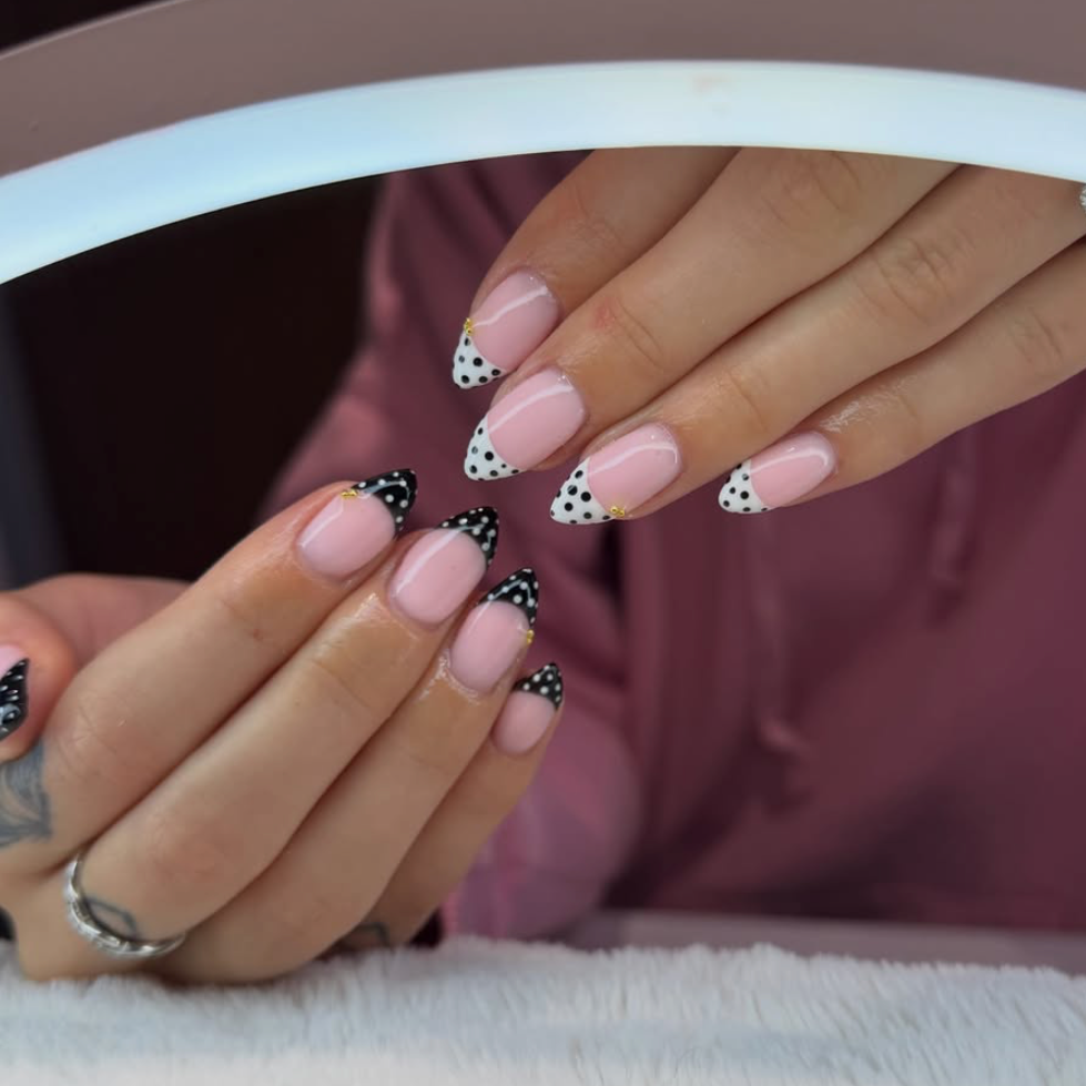 Close-up of a person's hands with manicured nails featuring black and white polka dot French tips.