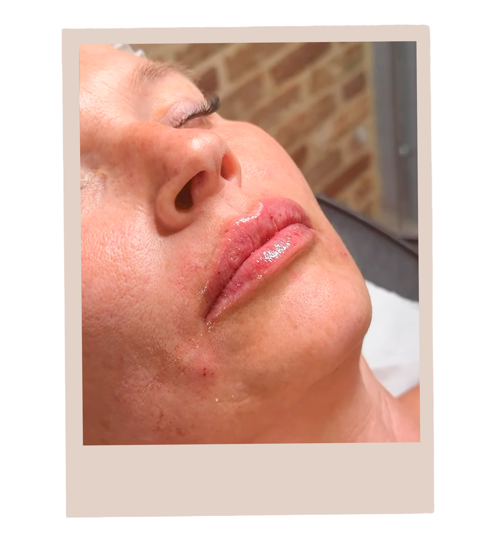 Close-up of a person's face with closed eyes, red lips, and slightly flushed skin, with a brick wall in the background.