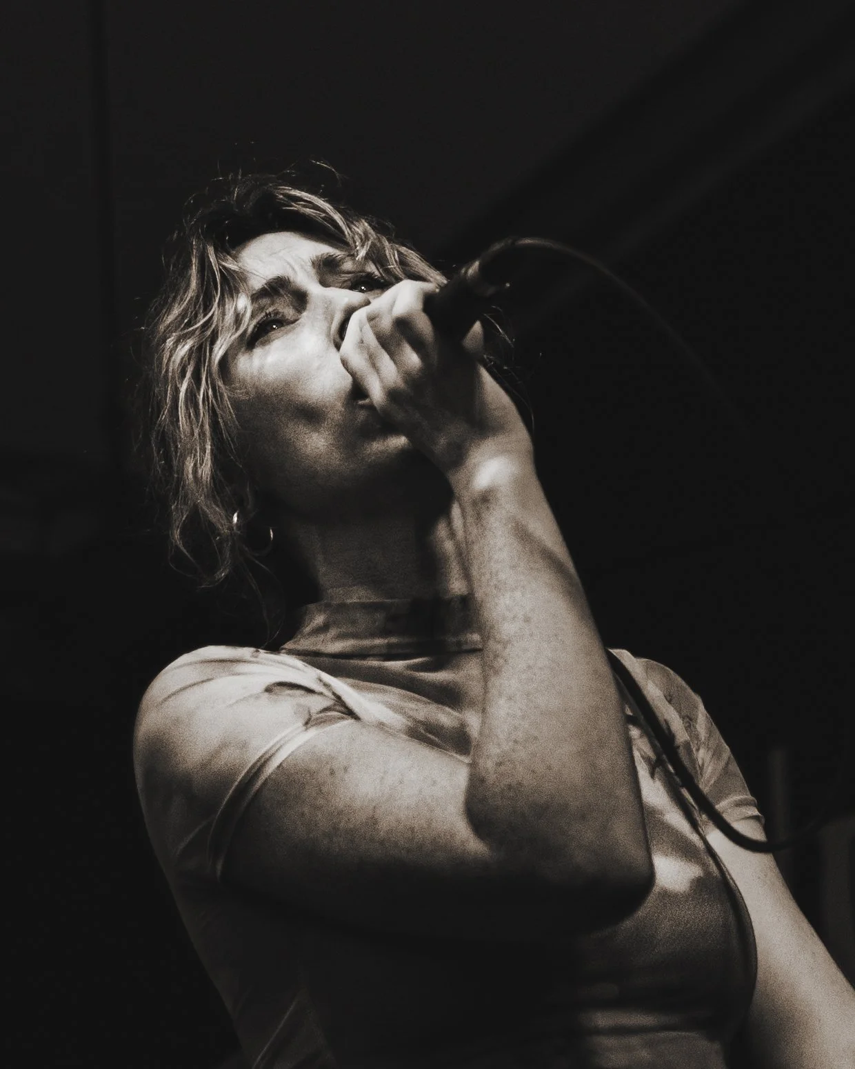 A black and white photo of a woman singing into a microphone, with short, wavy hair, looking emotional.