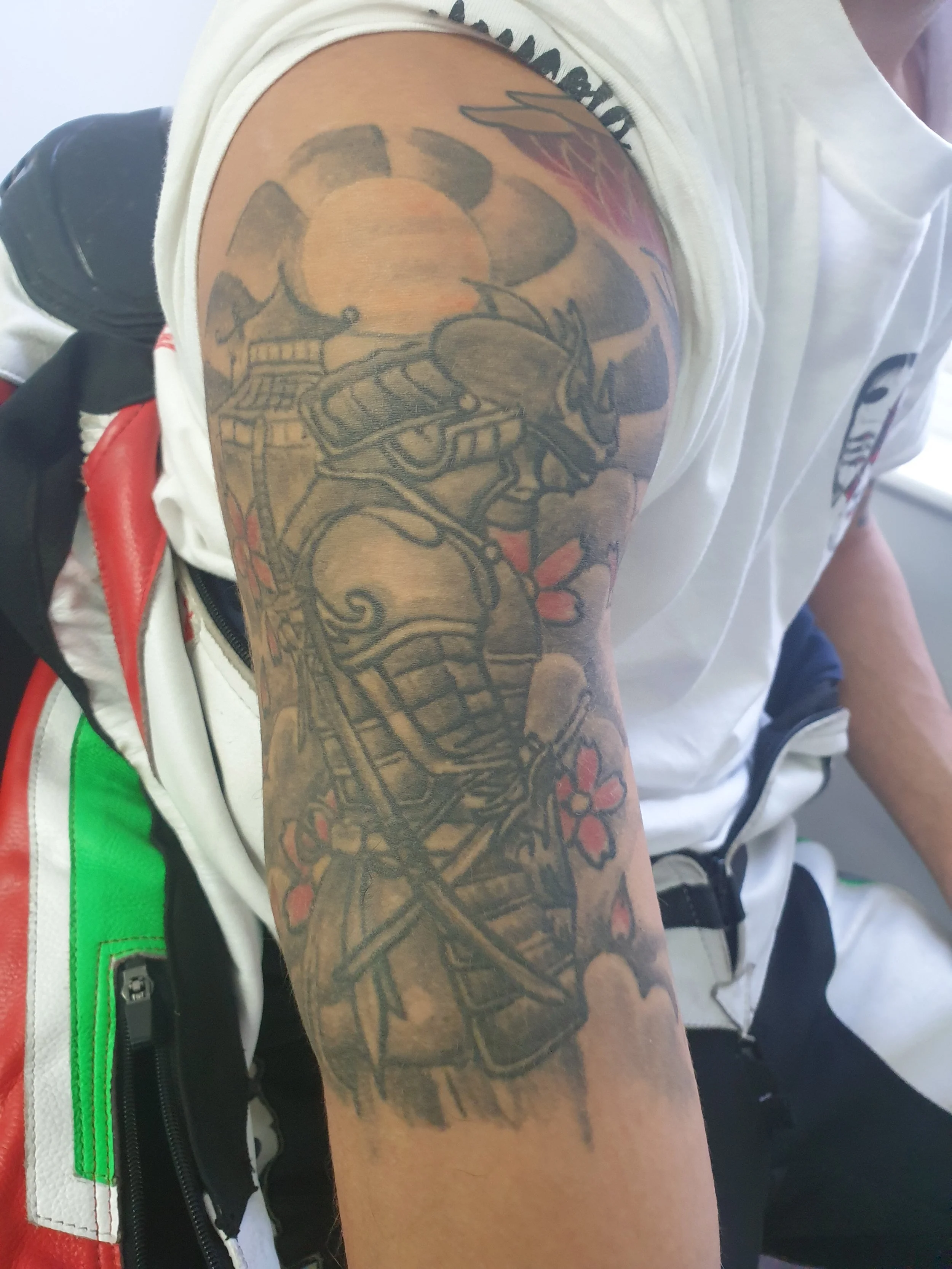 A tattoo on a person's upper arm features a detailed design with a skull holding a sword, surrounded by flowers and other decorative elements.