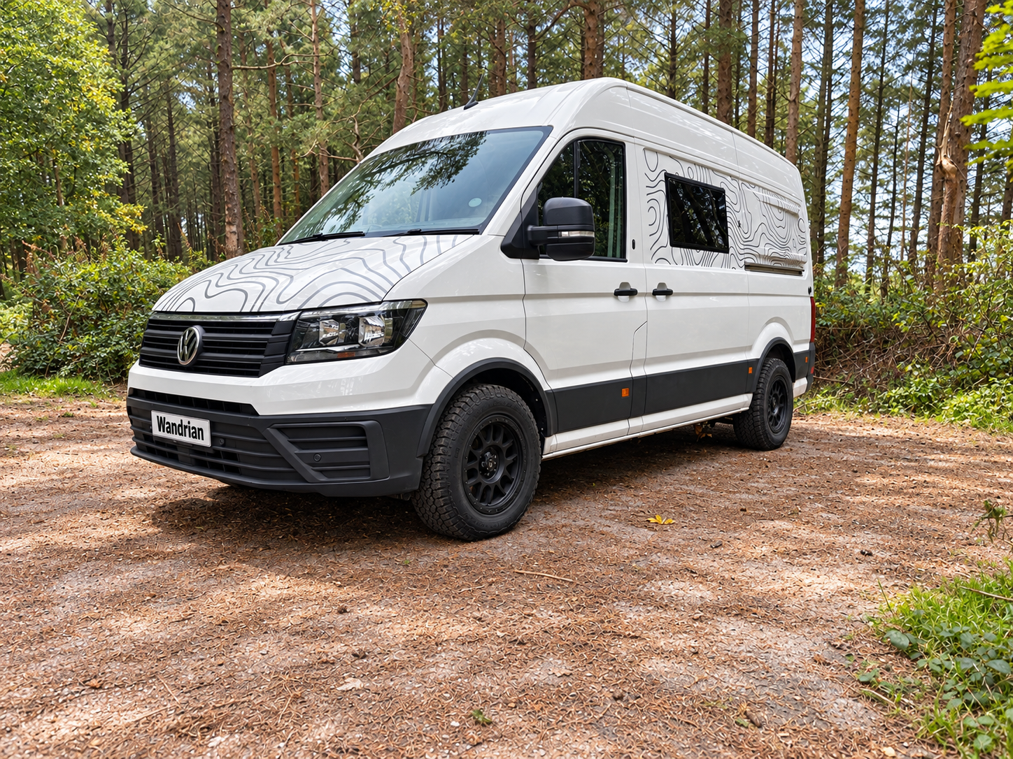 A white camper van parked on a dirt path in a forested area with trees and greenery in the background.