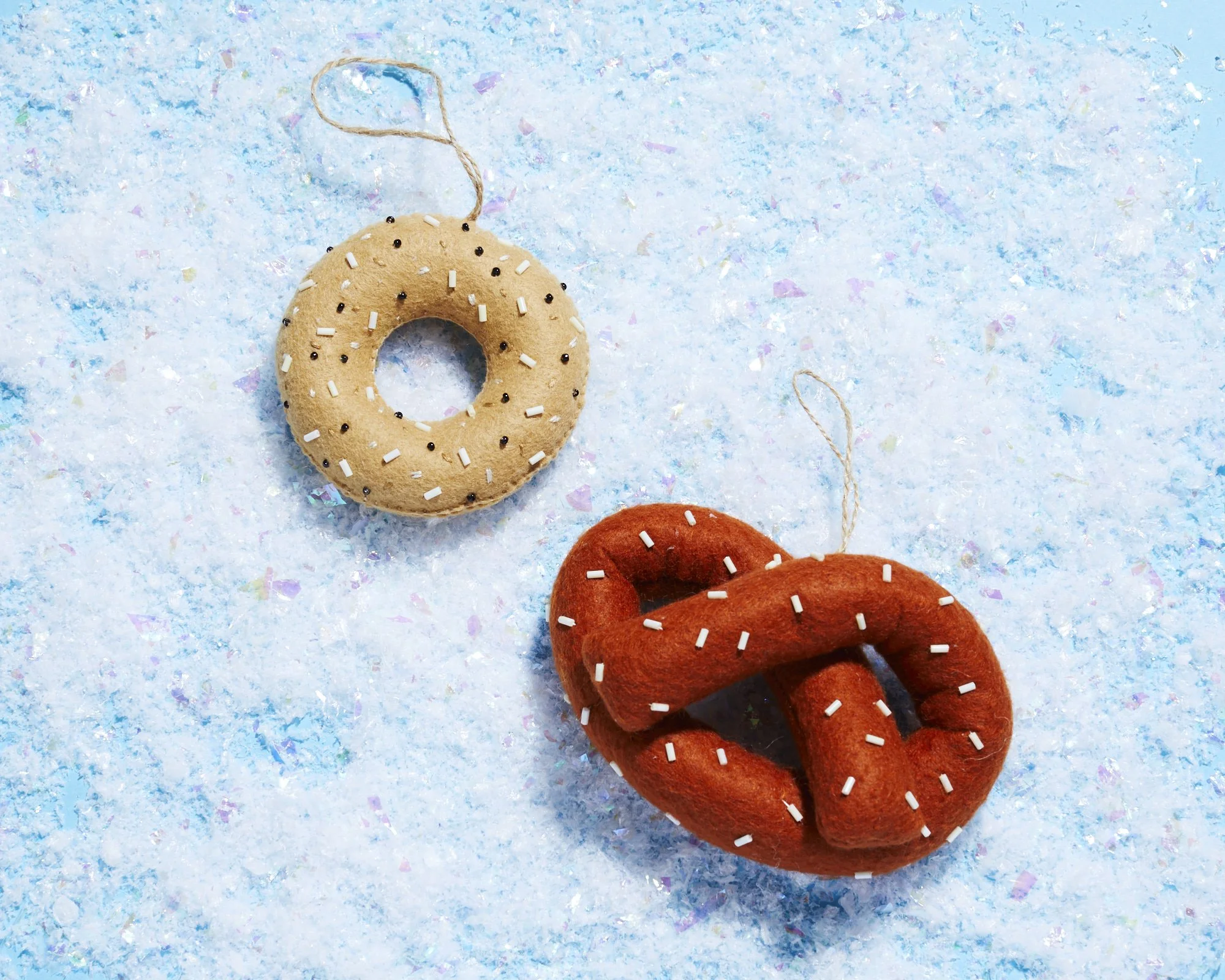 Felt everything bagel and salted pretzel ornaments on a snowy blue background