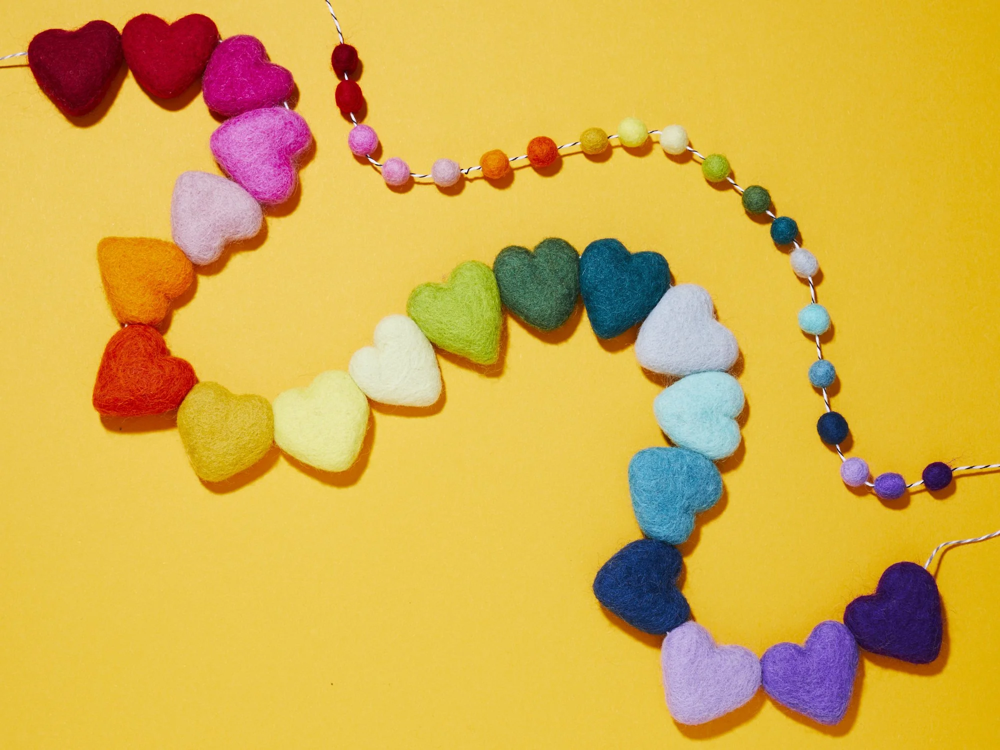 Colorful felt heart and pom-pom garland arranged on a bright yellow background