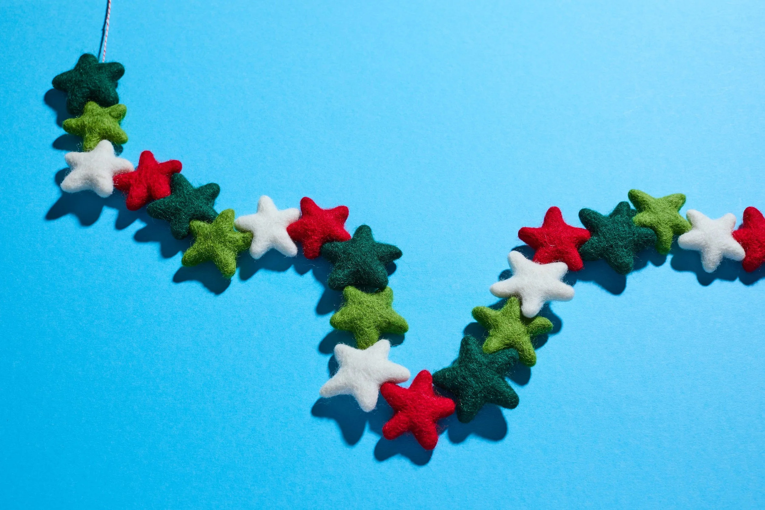 Colorful felt star garland in red, green, and white arranged on a bright blue background
