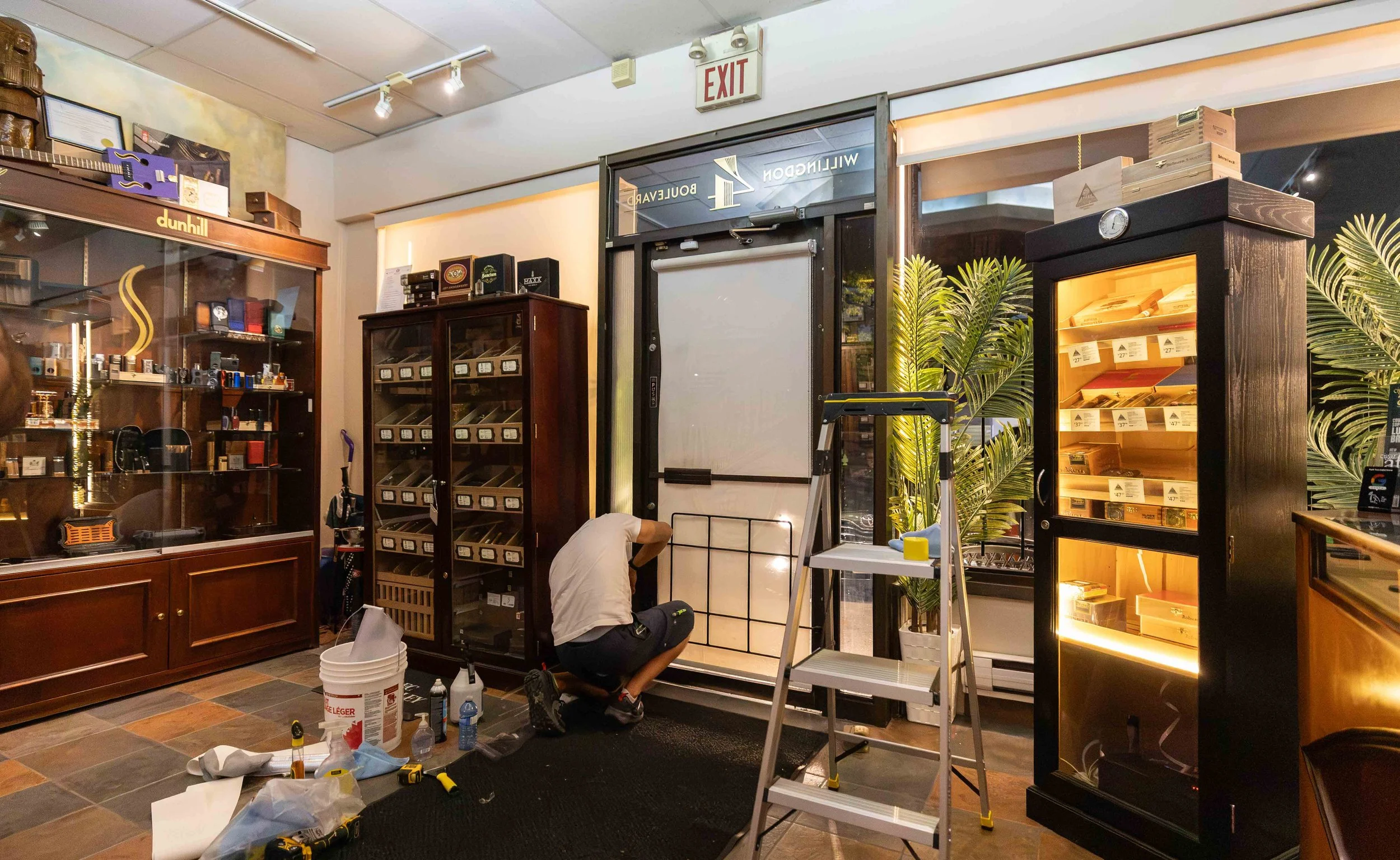 A person is working on assembling a display case in a retail store, surrounded by tools, supplies, and other display cabinets.