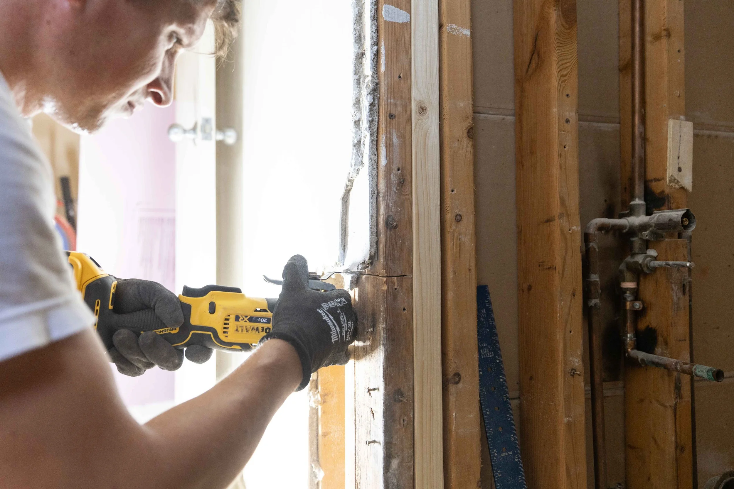 A person using a yellow power drill on wooden framing in a construction or renovation project.