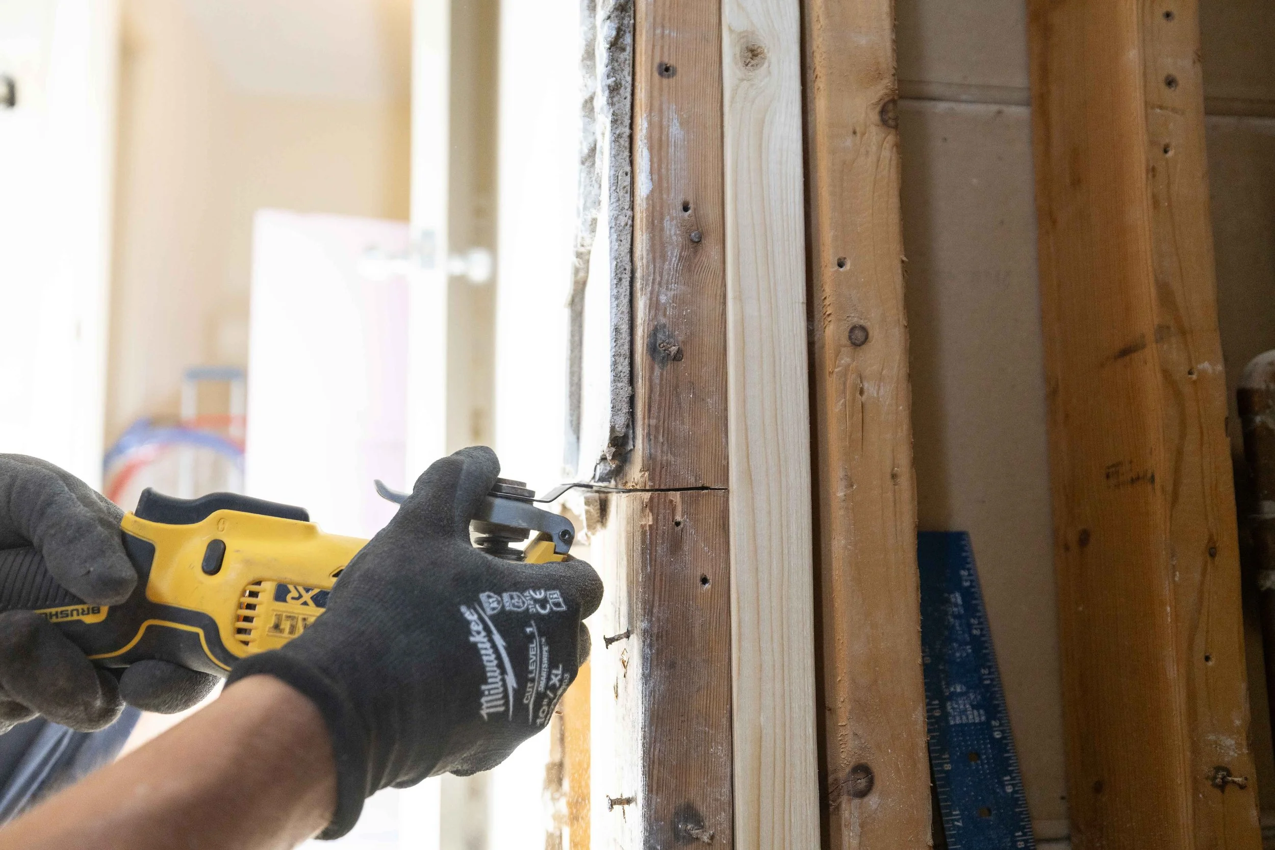 Person wearing a gray glove using a yellow reciprocating saw to cut a piece of wood on a construction site.