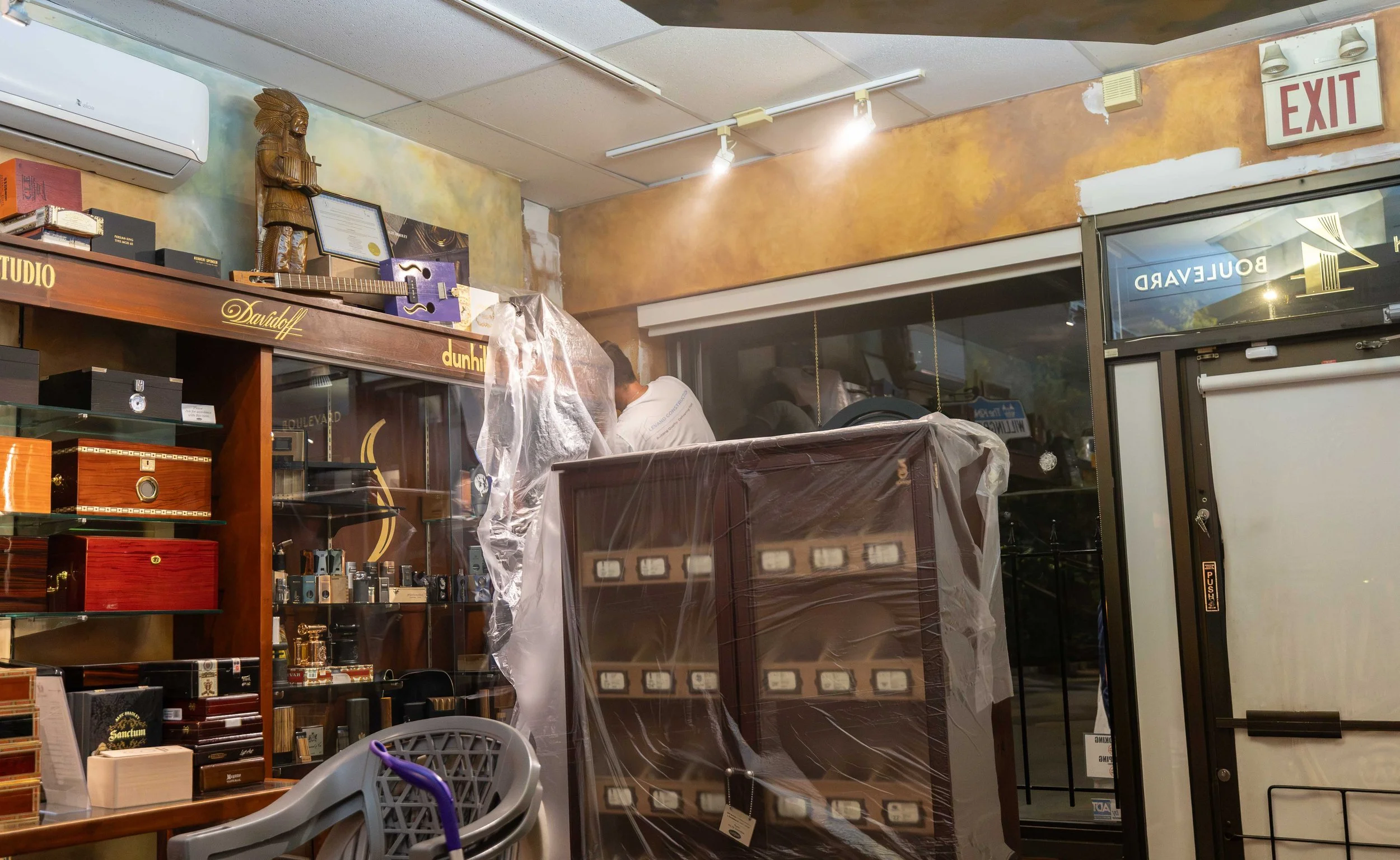 Store interior with shelves of cigar boxes, a guitar on a shelf, and a person with a plastic-covered item. Signage including 'EXIT' and 'BUIDLEAVARD' visible.