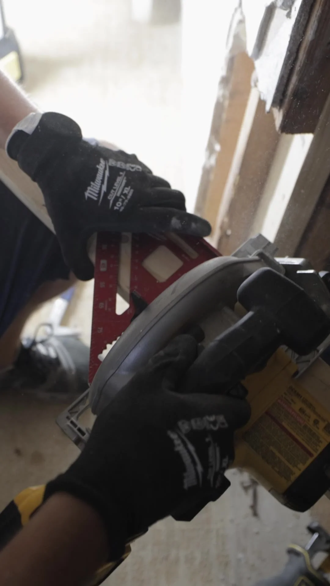 Gloved hands cutting a piece of lumber with a circular saw and a speed square during a bathroom renovation