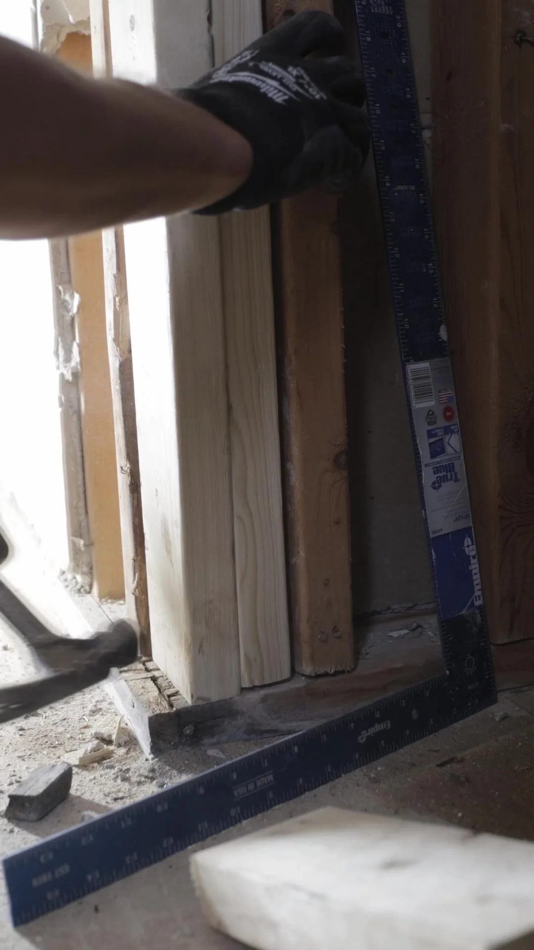 Crew member checking new wood framing with a framing square at the base of a bathroom wall in Etobicoke