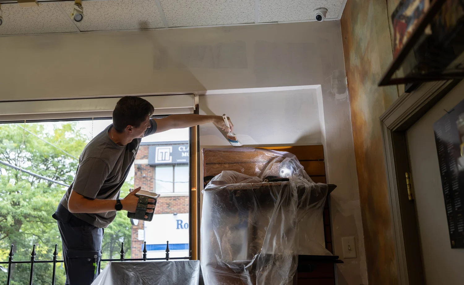 Painter working at a window wall with shop displays wrapped in plastic at Cigar Studio, Etobicoke