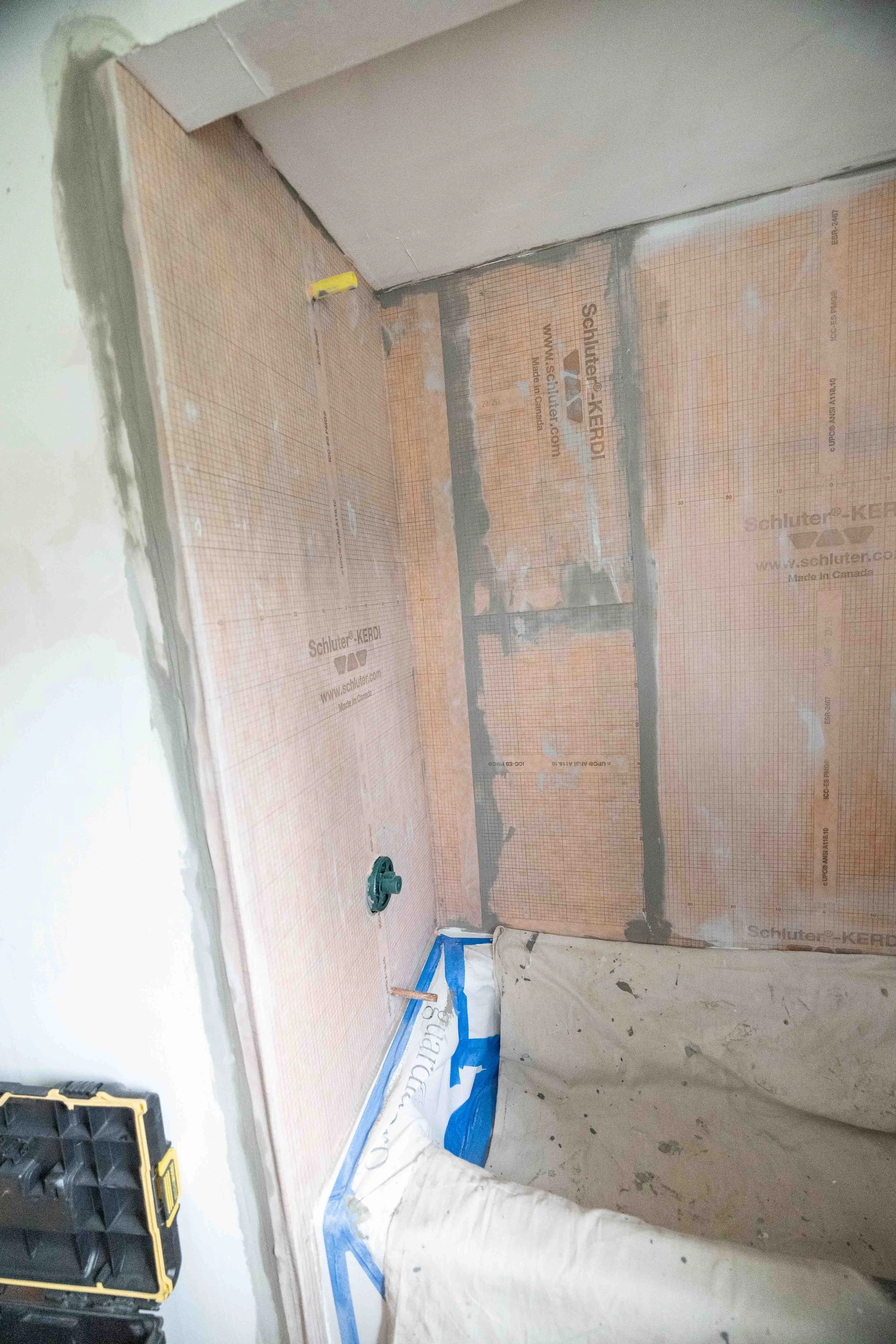 Interior wall under construction with insulation and drywall partially installed, tools and construction materials visible on the floor.