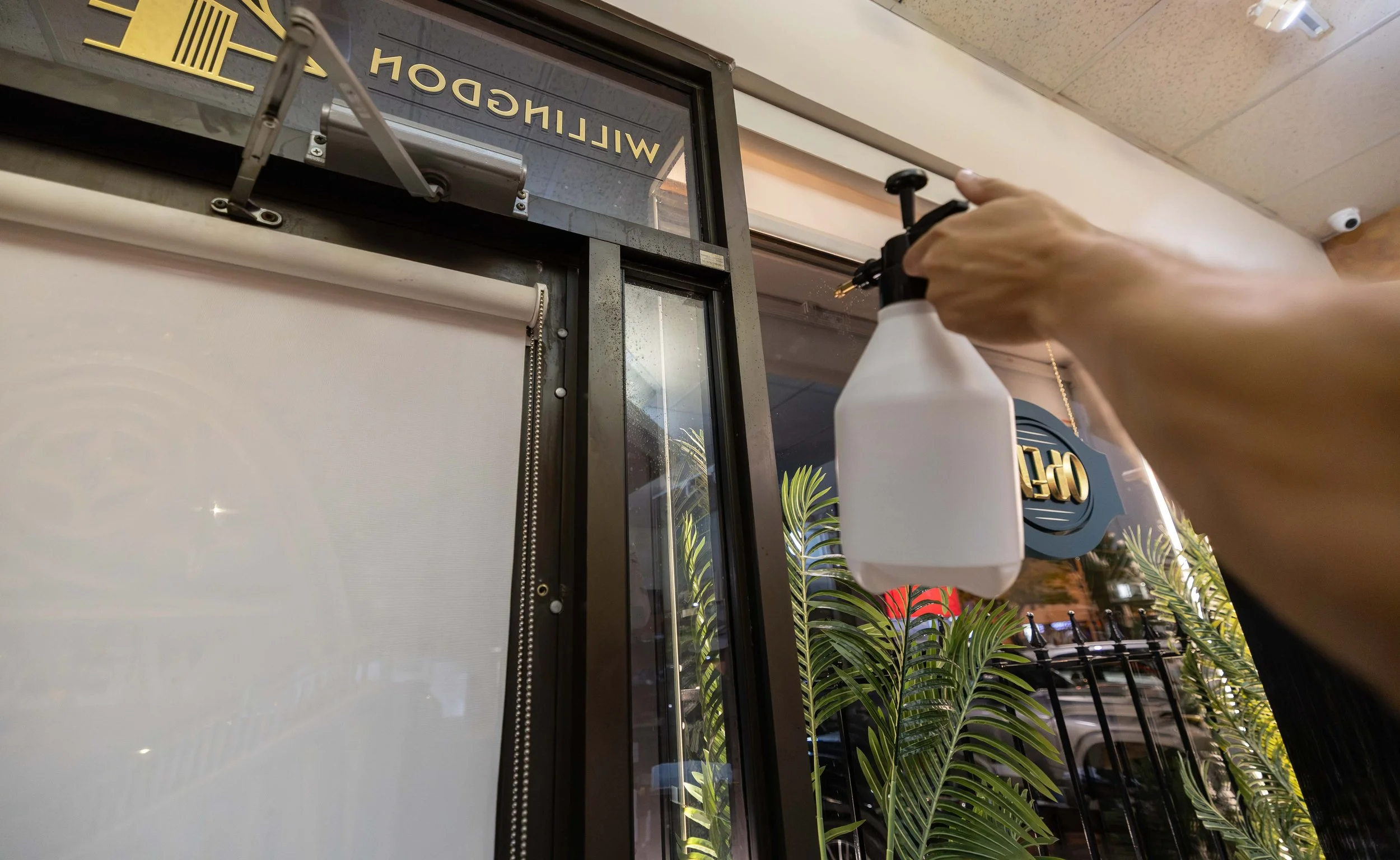A person using a spray bottle to clean a glass window at a Willy's Donut Shop.