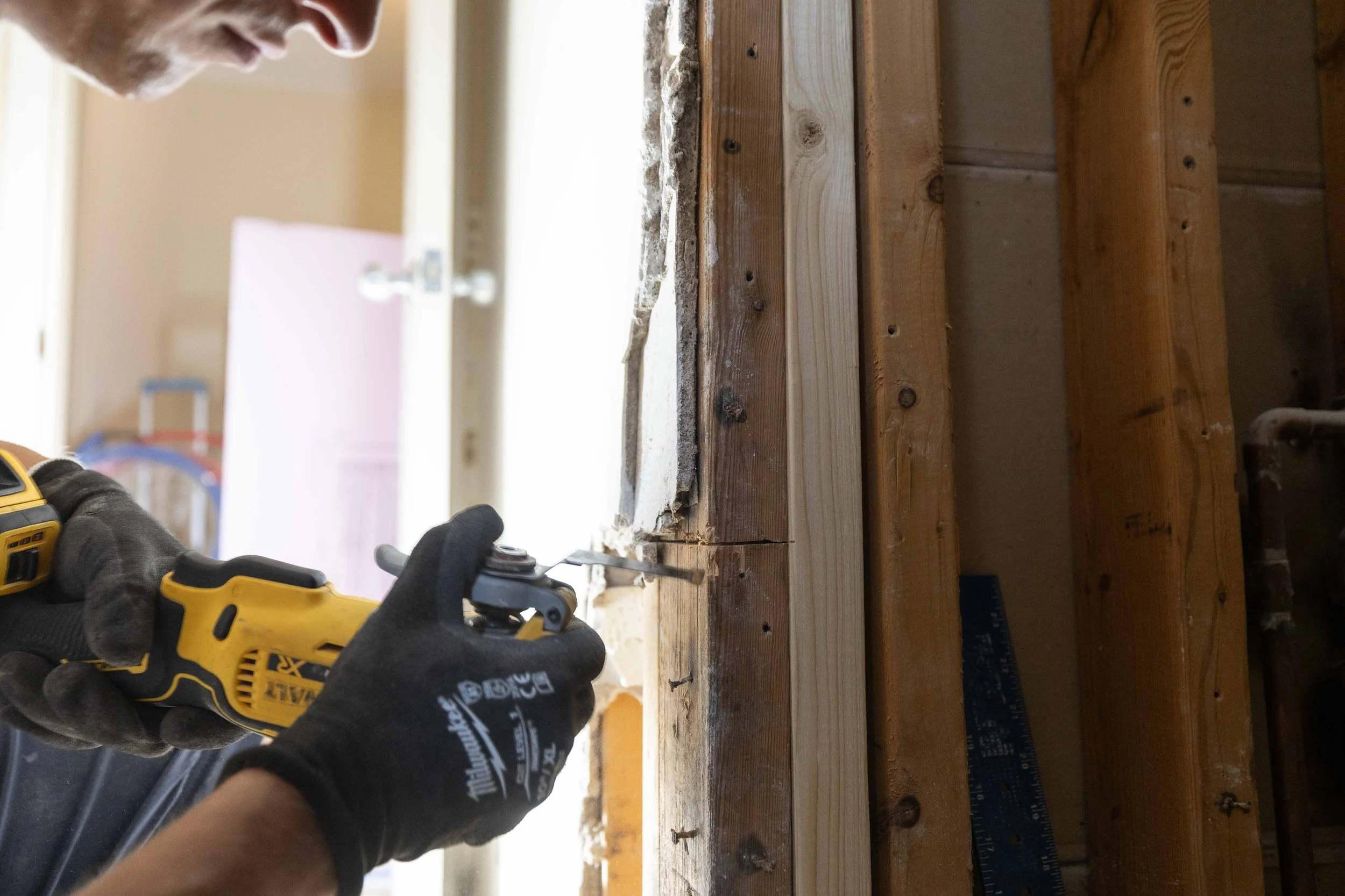 Person using a yellow cordless drill to work on a wooden surface, wearing black gloves.