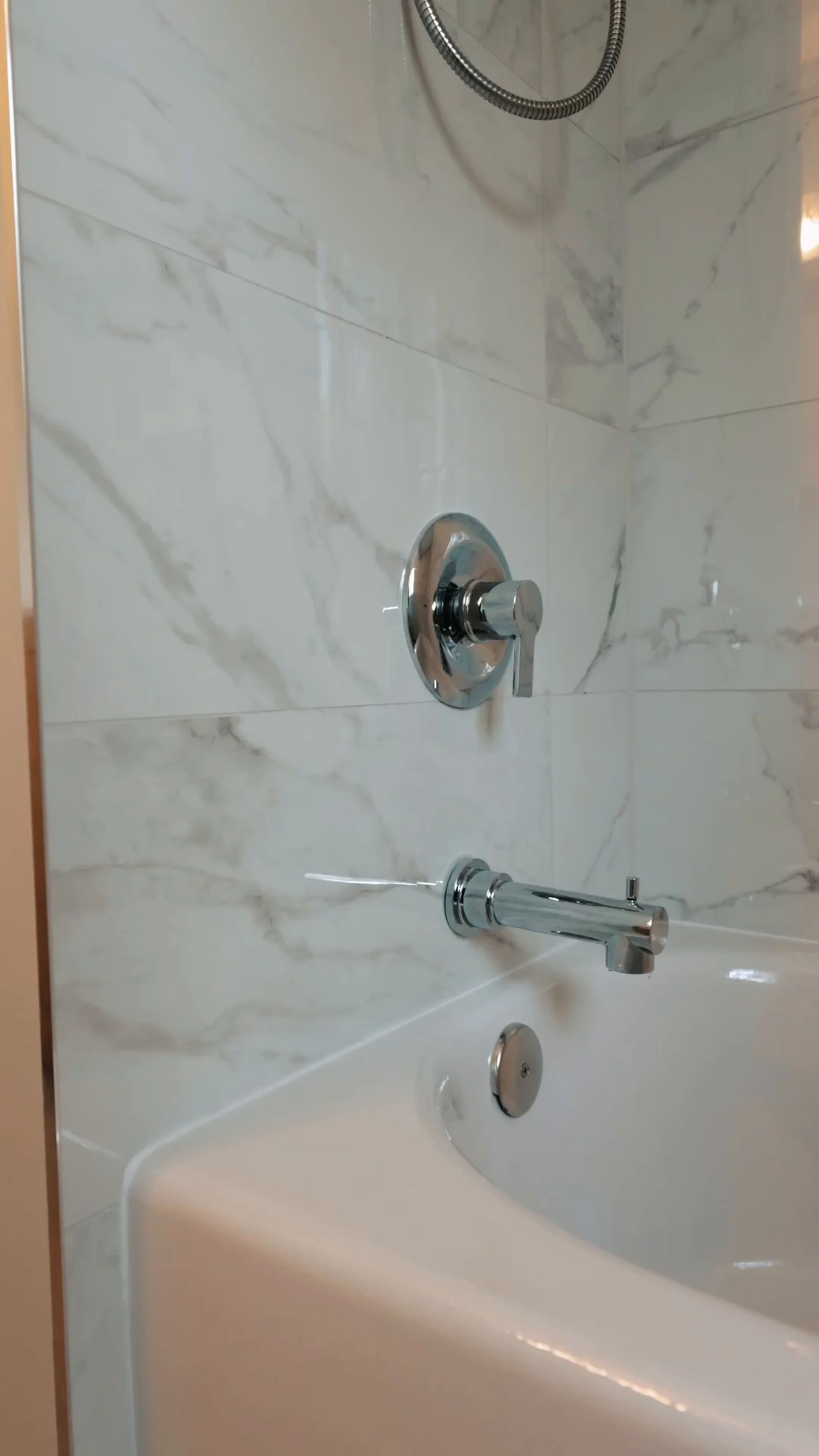 New white bathtub with chrome shower controls and marble-look tile surround in a renovated Etobicoke bathroom