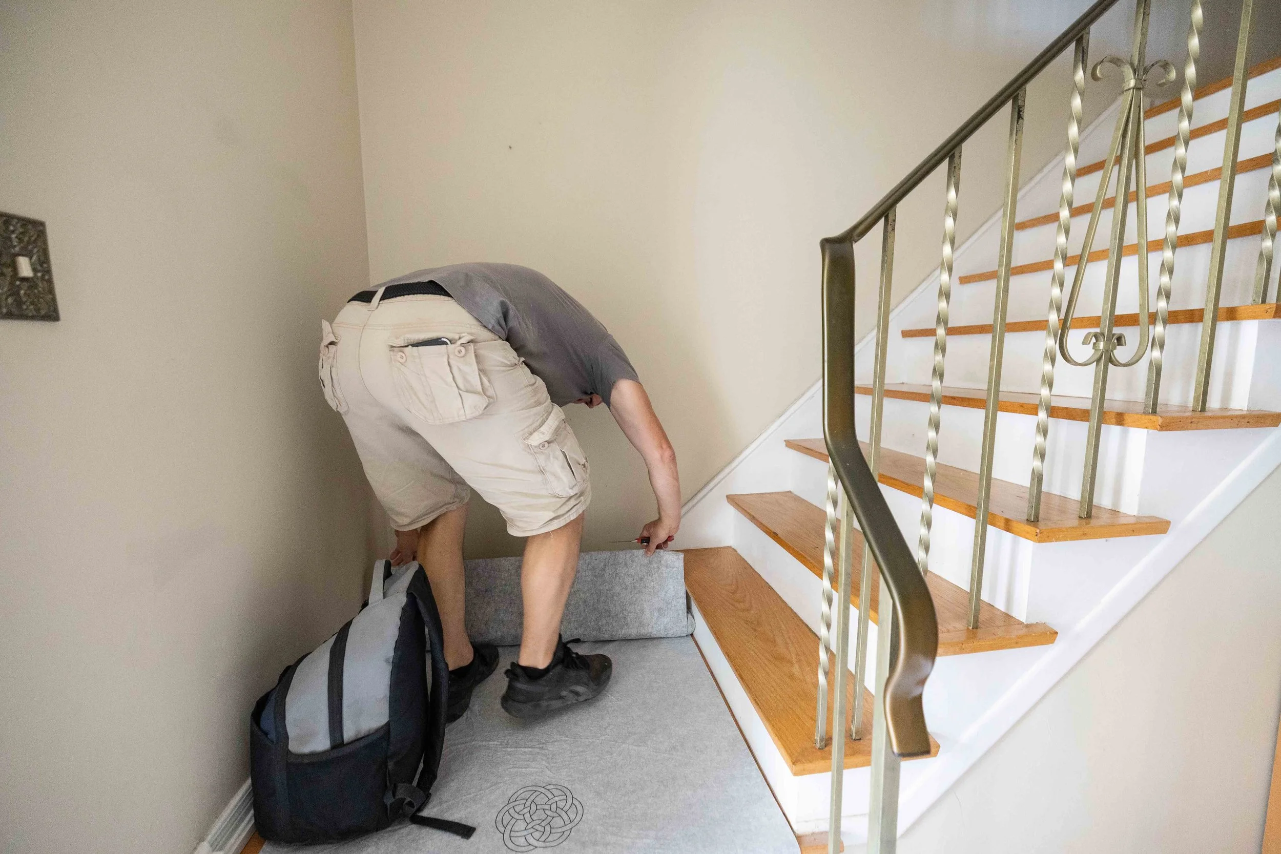 Person bending down to place or pick up a backpack at the bottom of a staircase in a house.