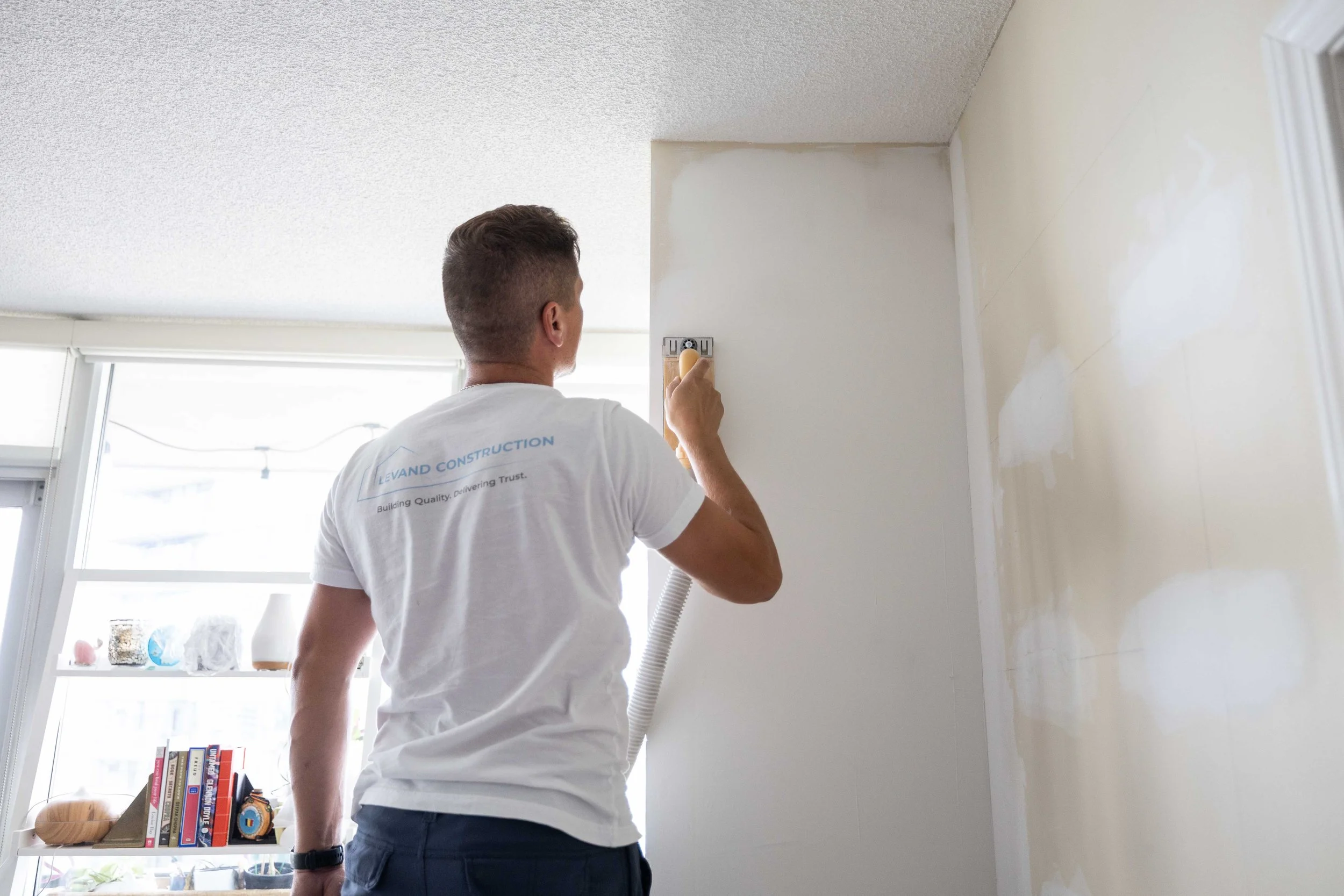 A man is painting a wall with a roller brush in a sunny room.