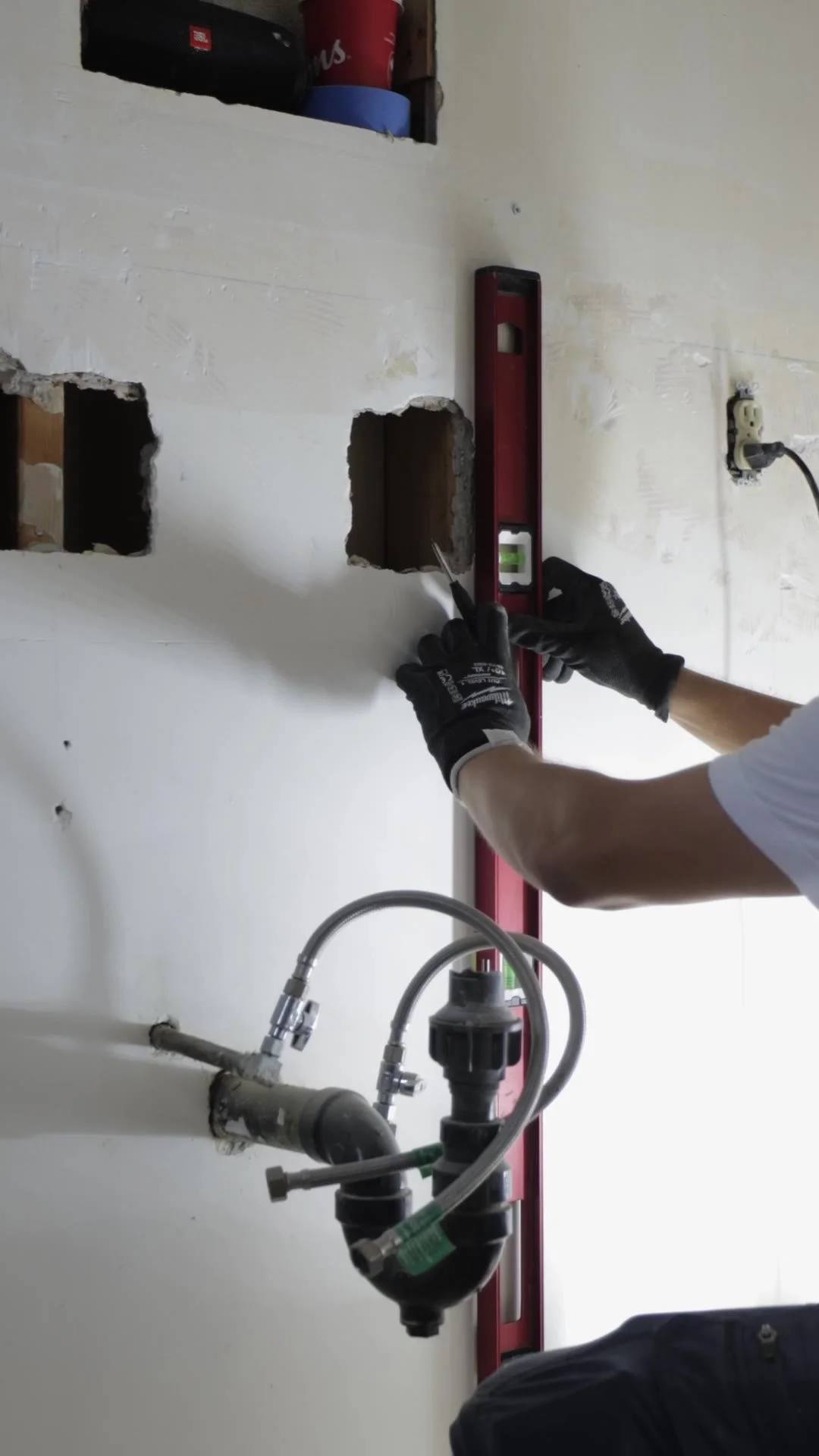 Crew member holding a long level against a bathroom wall next to the plumbing rough-in during a renovation in Etobicoke