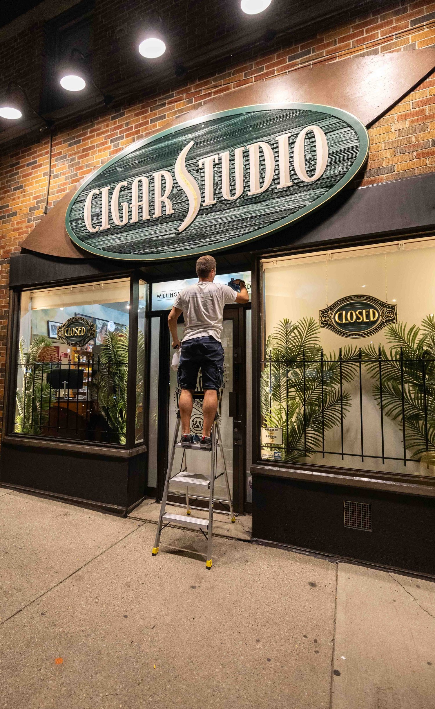 Levand Construction crew member on a ladder at the Cigar Studio storefront in Etobicoke at night